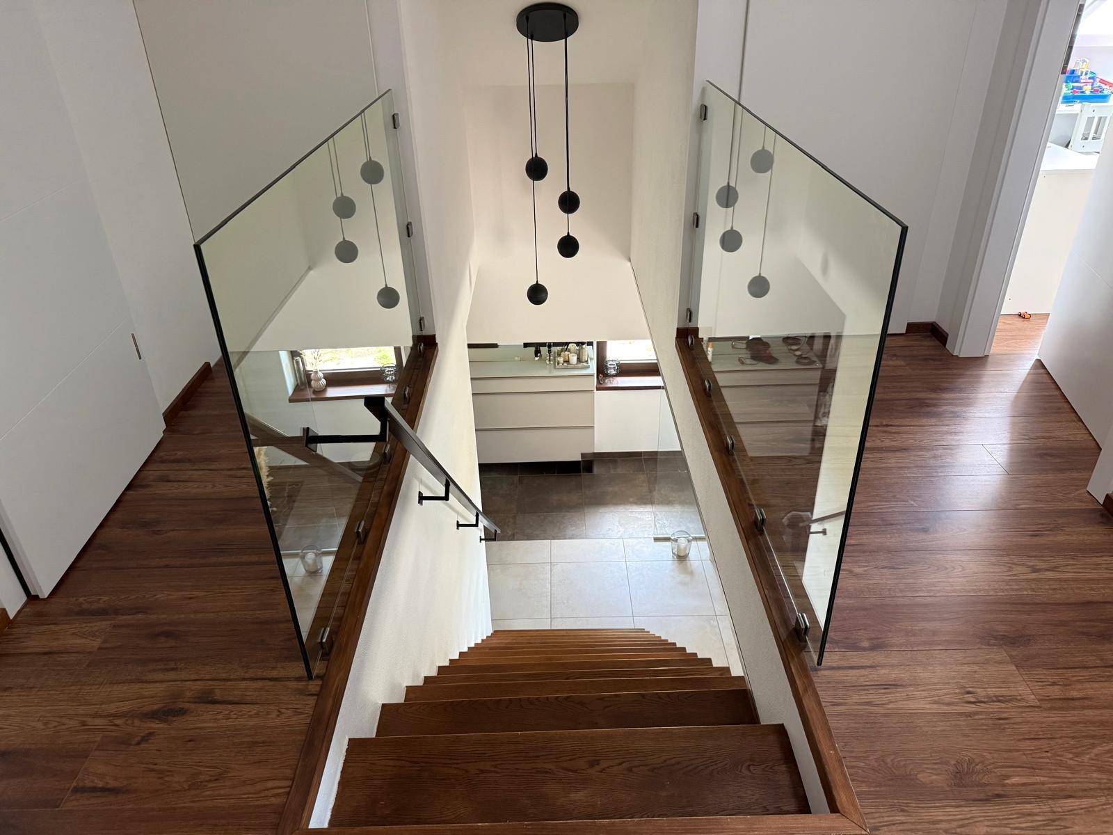 Elegante Holztreppe mit Glasgeländer und moderner Hängeleuchte.