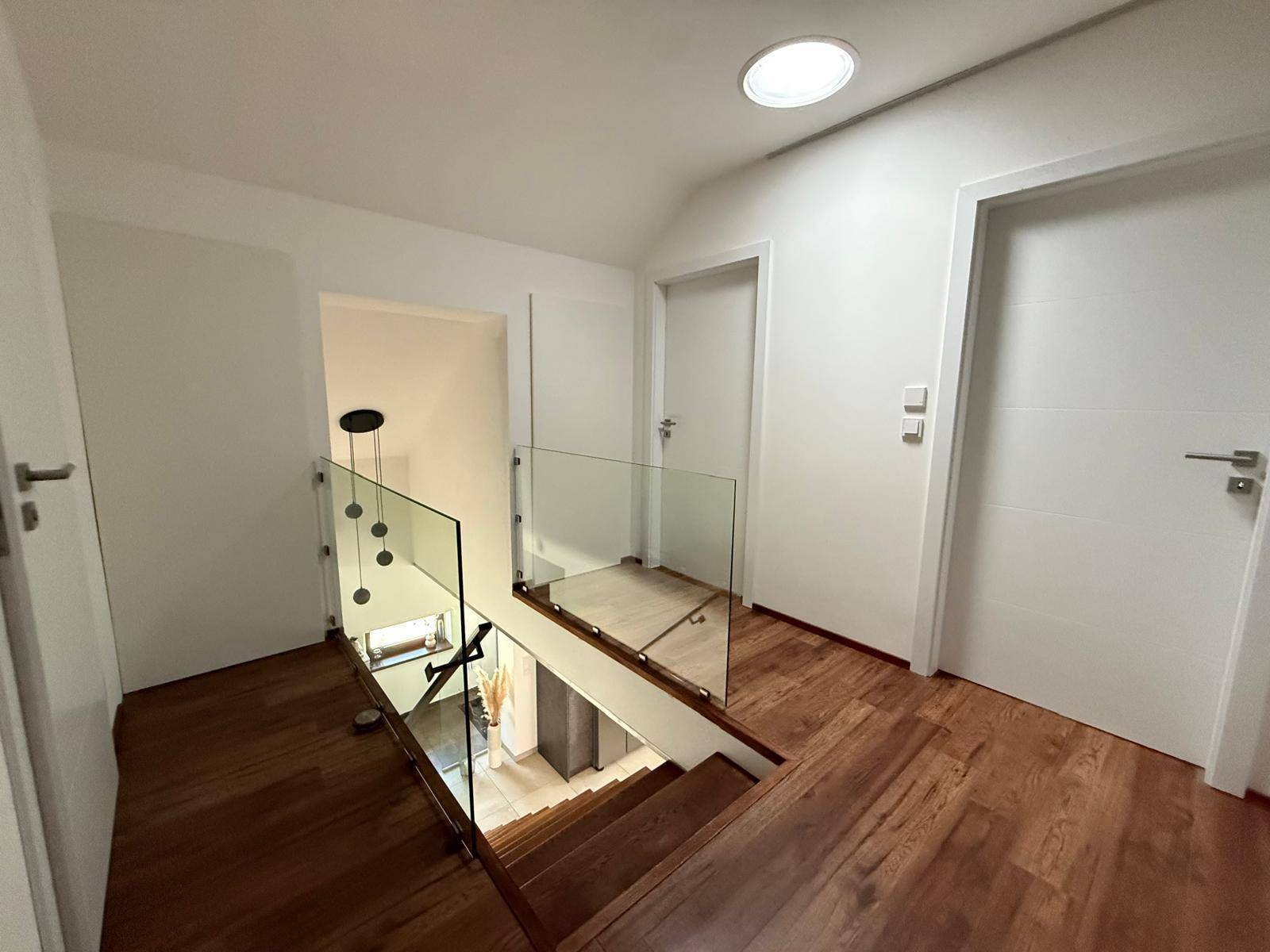 Heller Flur mit Holztreppe, Glasgeländer und modernen Türen.