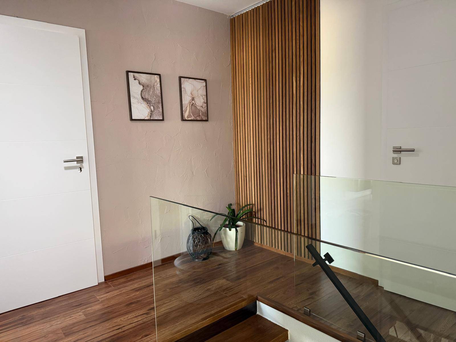 Moderner Flur mit Holzfußboden, Glasgeländer und dekorativer Holzvertäfelung an der Wand.