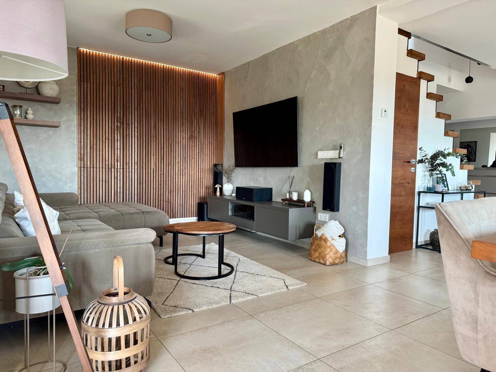 Modernes Wohnzimmer mit beigem Sofa, Holzwandverkleidung und Flachbildfernseher.