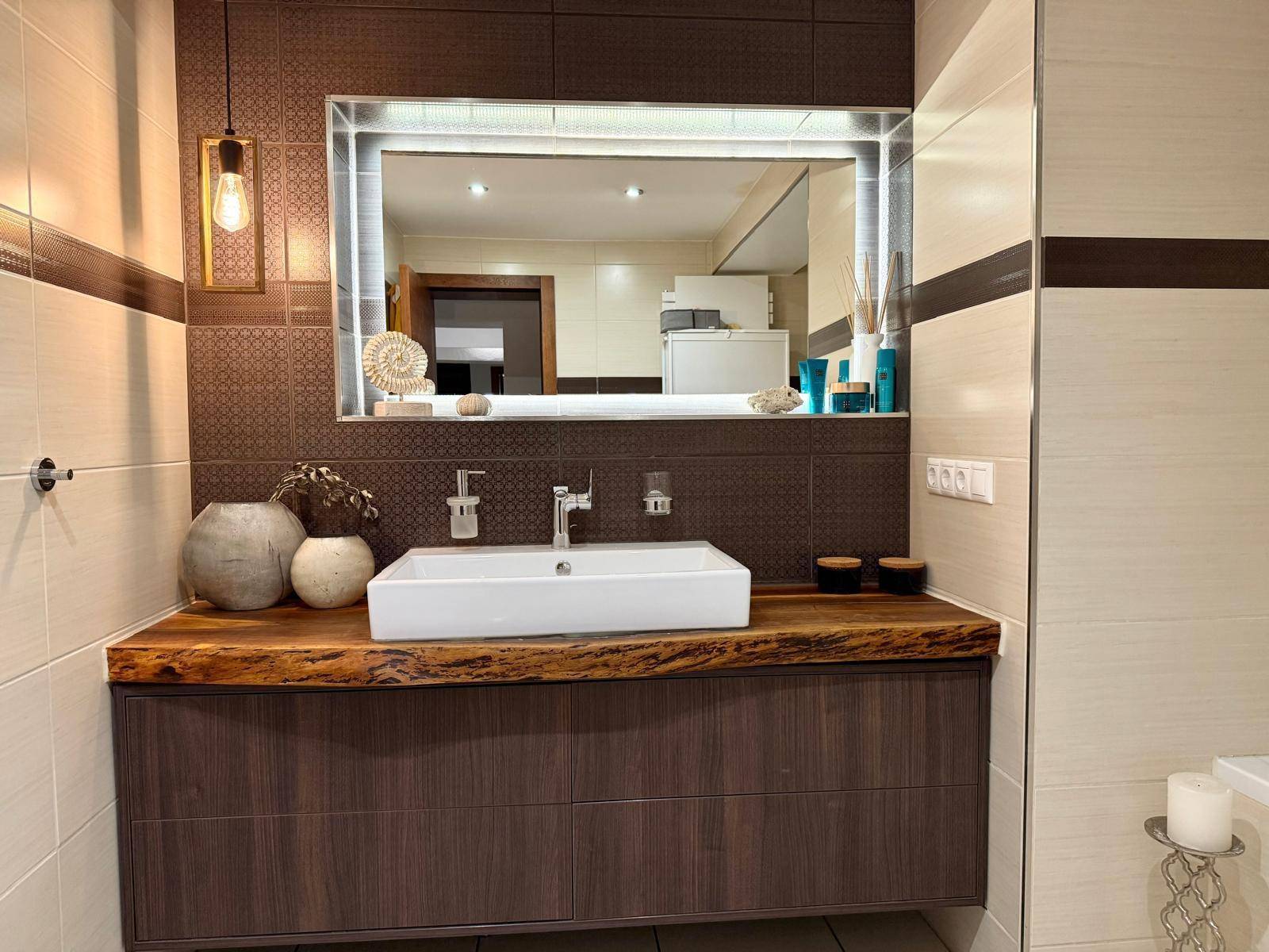 Elegantes Badezimmer mit großem Waschtisch, beleuchtetem Spiegel und Holzakzenten.