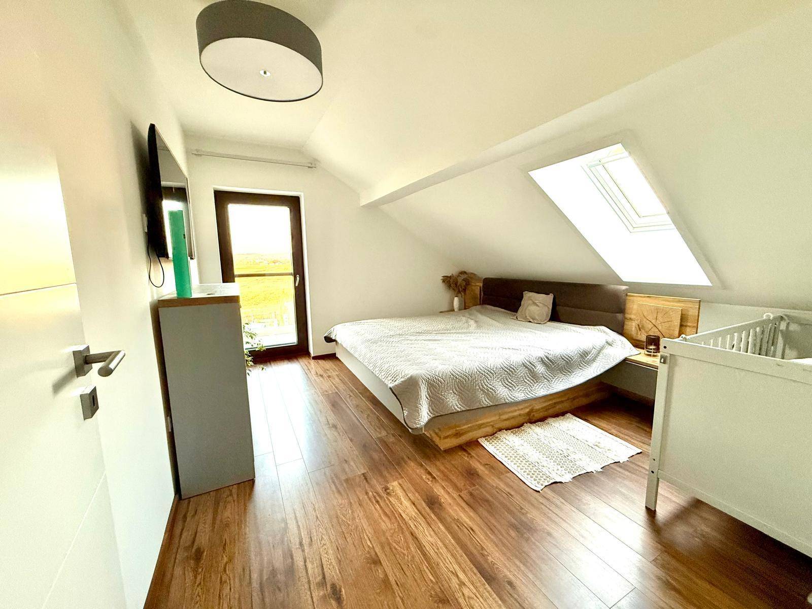 Gemütliches Schlafzimmer im Dachgeschoss mit Holzboden, Dachfenster und Babybett.