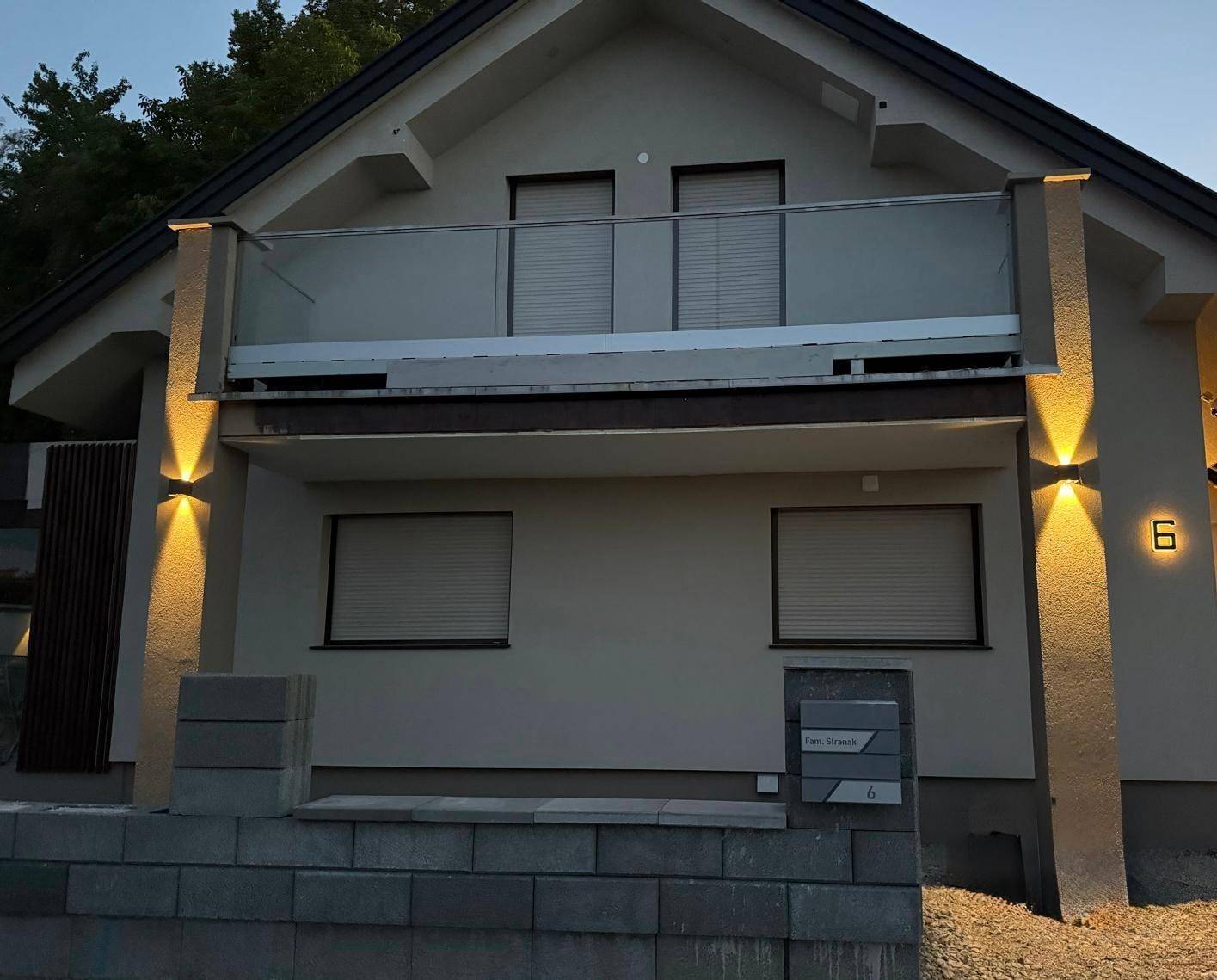 Modernes Einfamilienhaus bei Nacht mit beleuchteter Fassade und Balkon.