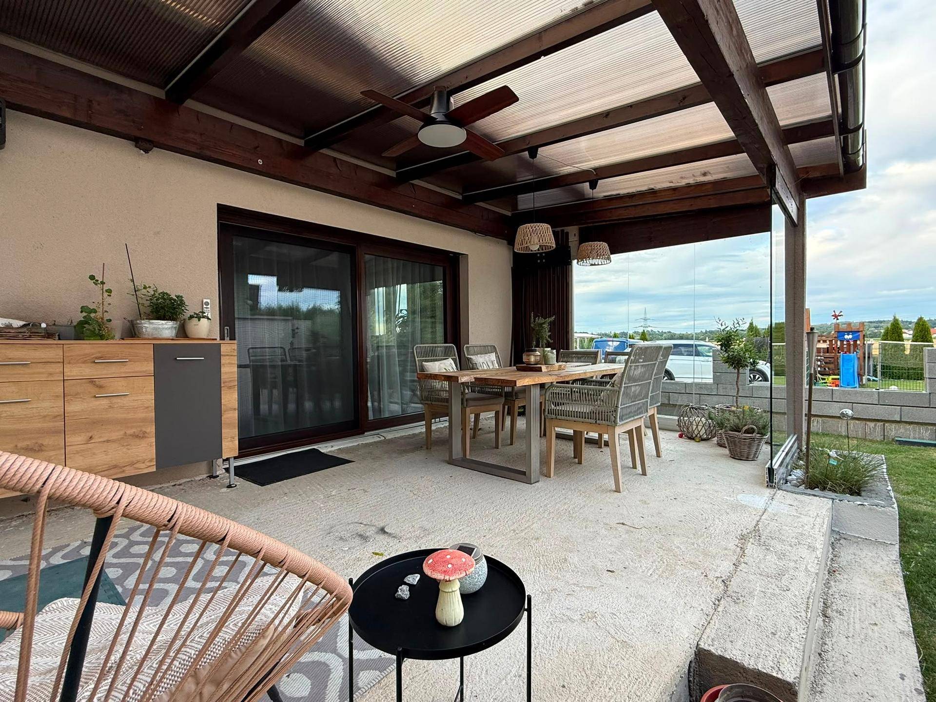 Überdachte Terrasse mit Essbereich, Deckenventilator und Blick ins Grüne.
