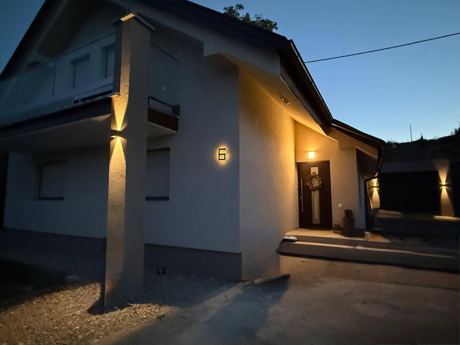 Modernes Haus bei Nacht mit beleuchteter Fassade und Eingangsbereich.