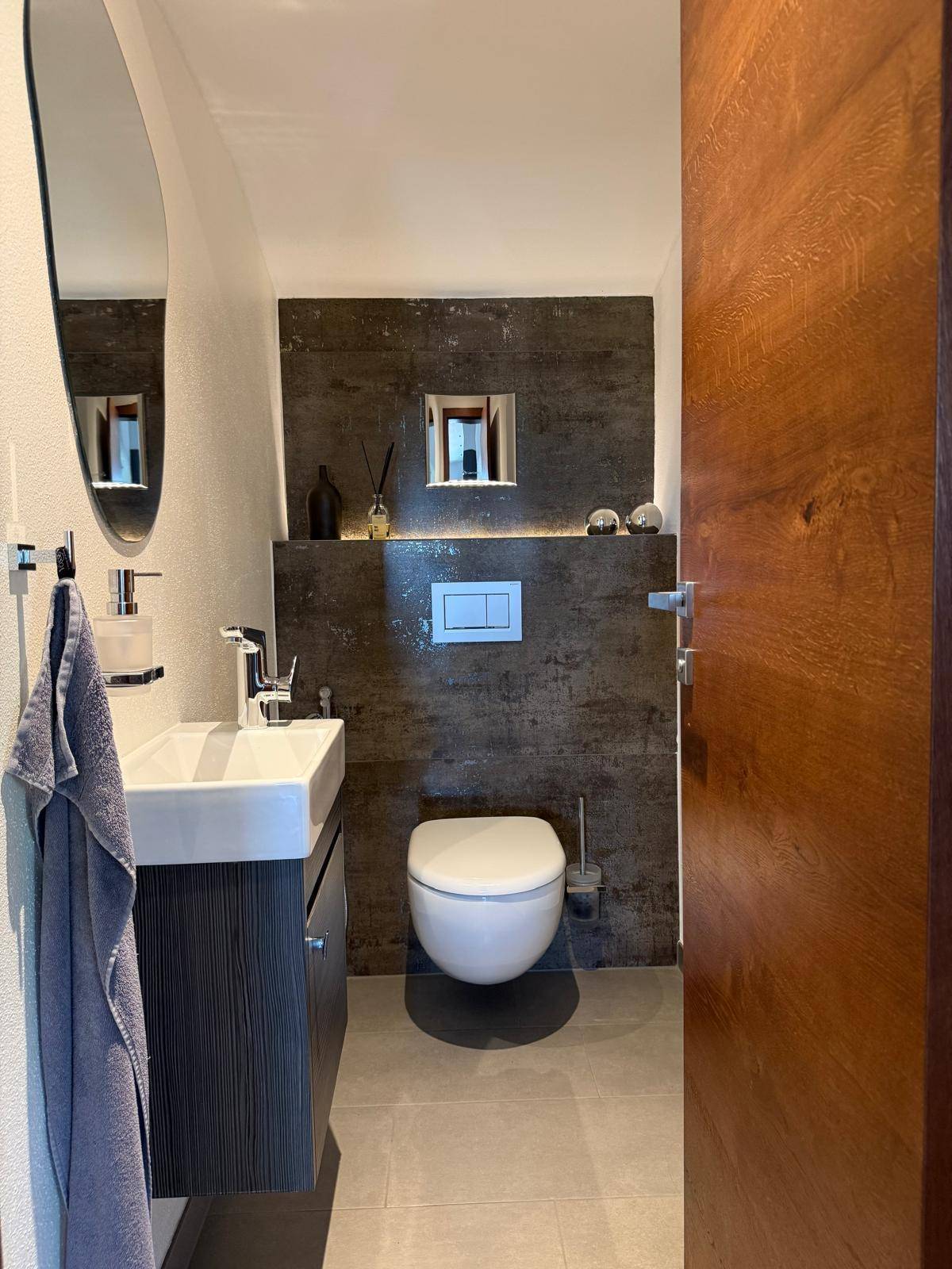 Stilvolles Gäste-WC mit Wand-WC, kleinem Waschbecken und dunklen Fliesen.