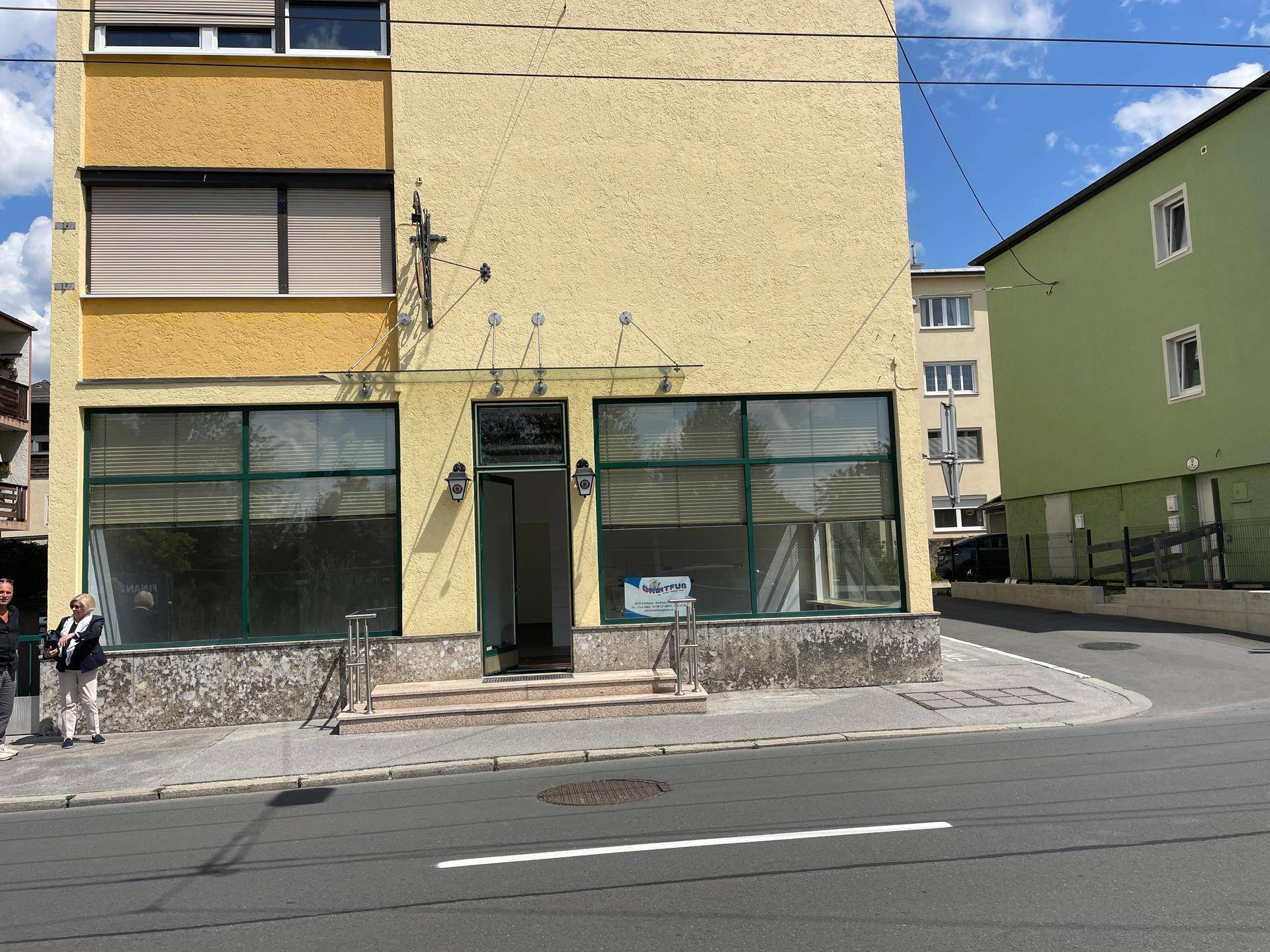 Ansicht des gelben Geschäftsgebäudes von der Straße mit angrenzendem grünen Gebäude und klarem Himmel.