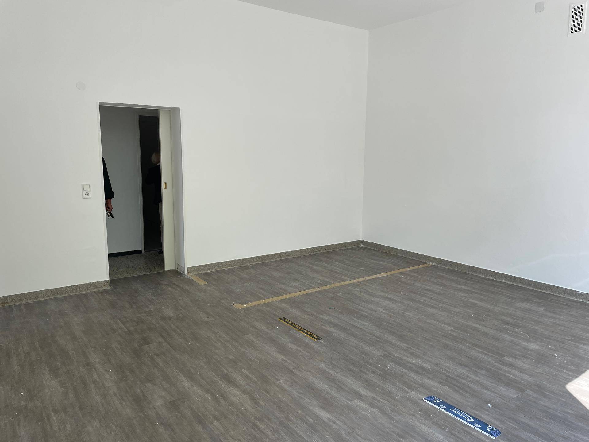 Geräumiger, leerer Raum mit weißen Wänden und modernem Vinylboden, ideal für gewerbliche Nutzung.