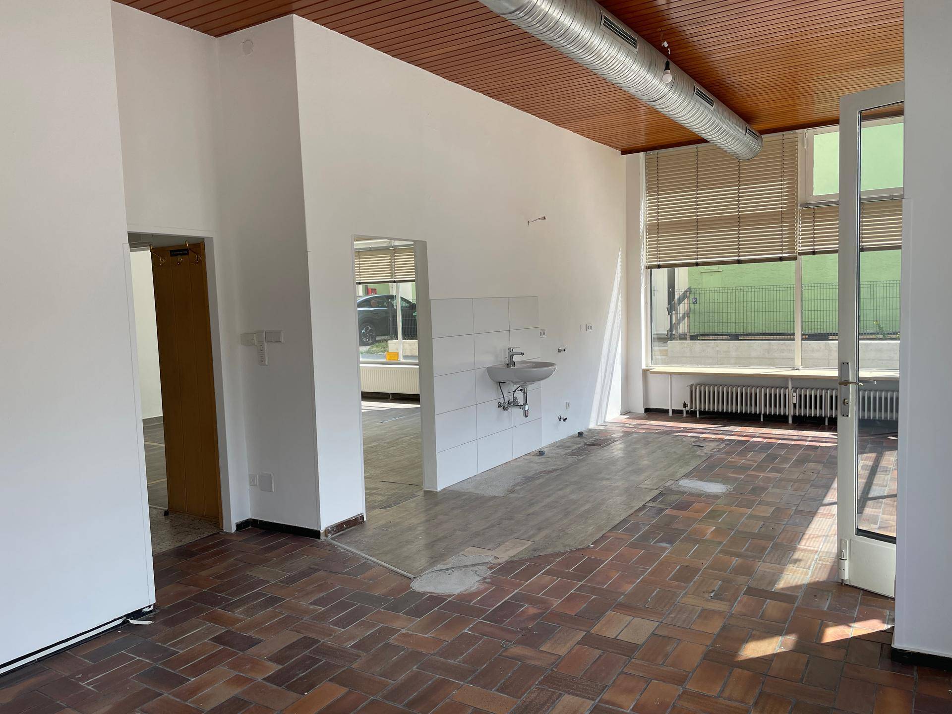 Geräumiger, leerer Geschäftsraum mit Terrakotta-Fliesenboden und Holzdecke, bereit zur Renovierung.