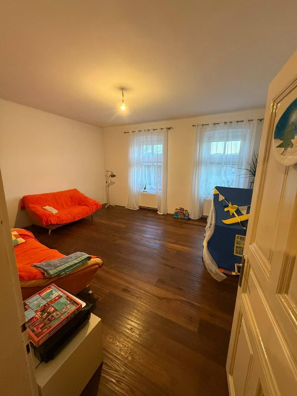 Helles Zimmer mit dunklem Holzboden und zwei orangefarbenen Sofas, bereit zur individuellen Gestaltung.