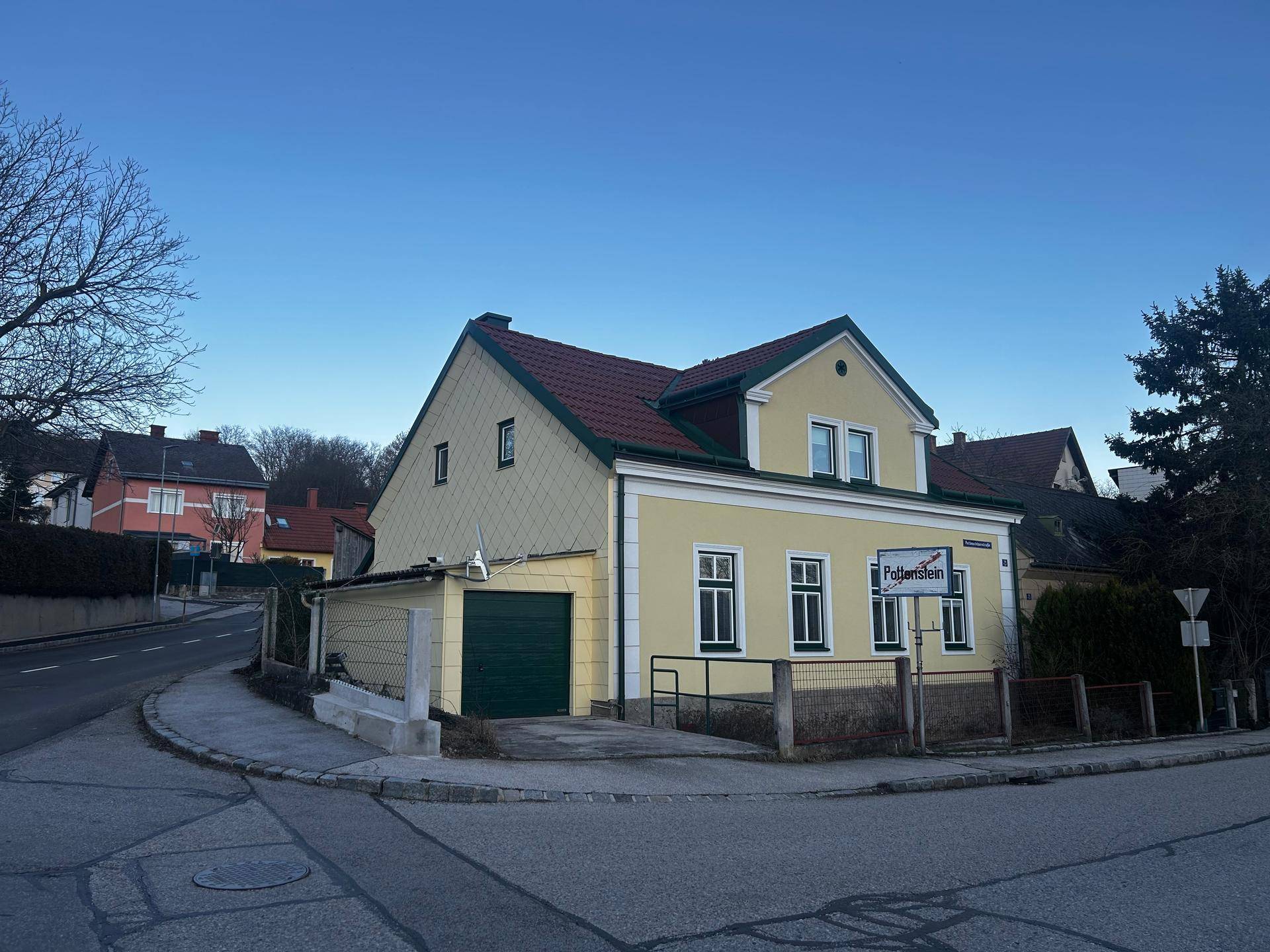 Ansicht des gelben Hauses mit rotem Dach und integrierter Garage von der Straßenseite.
