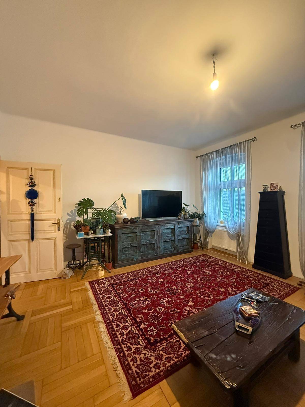 Gemütliches Wohnzimmer mit Fischgrätparkett, großem Teppich und einem Fenster mit Vorhängen.