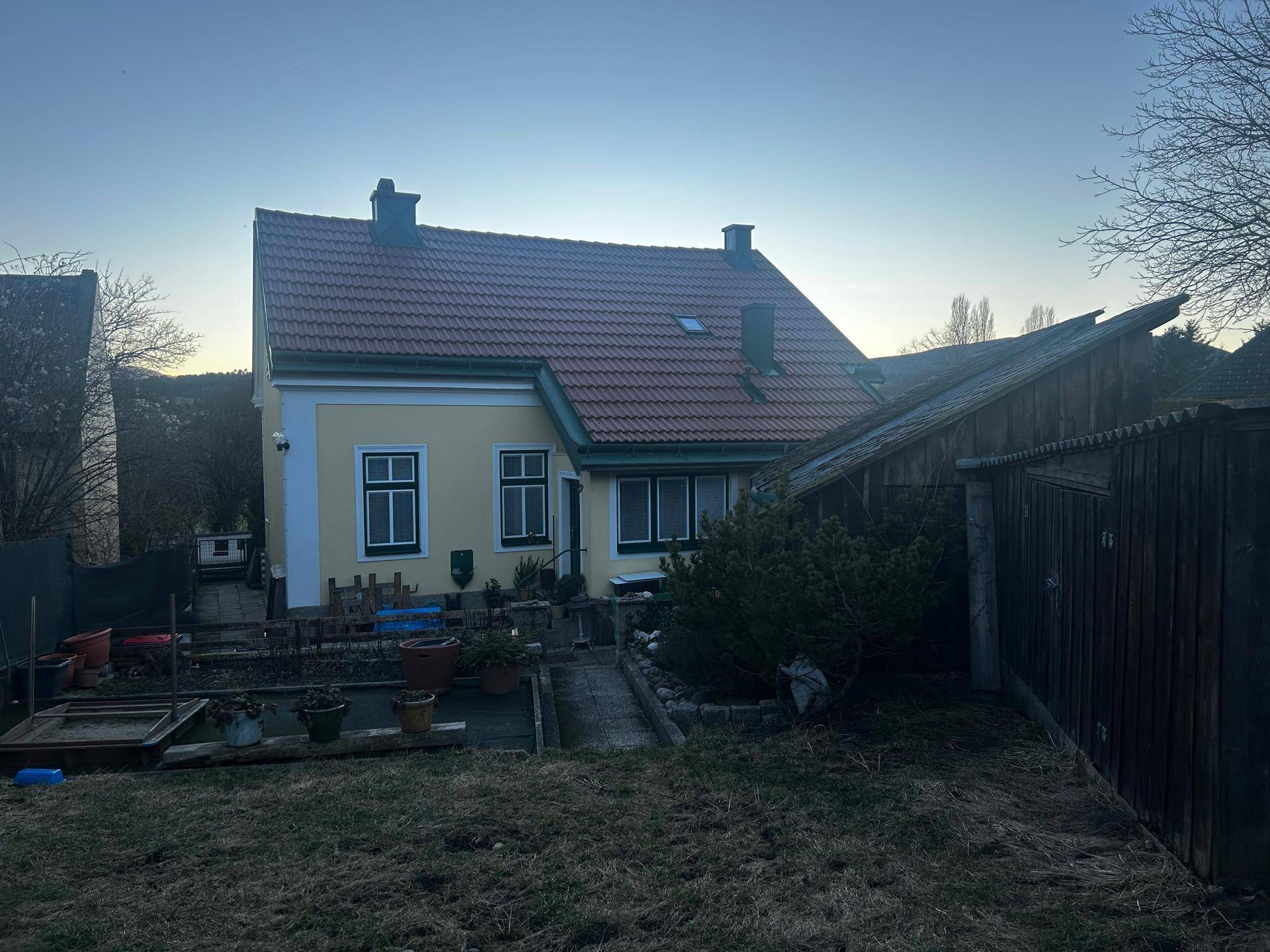 Hinteransicht des Hauses mit einem Gartenbereich, Pflanzen und einem Holzschuppen.