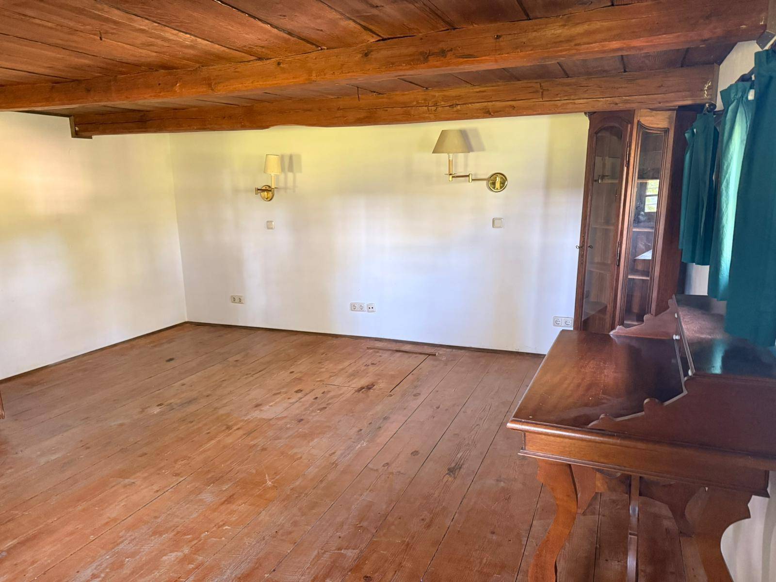 Geräumiger Raum mit Holzbalkendecke und breiten Dielen, ausgestattet mit Wandleuchten und einem Schrank.