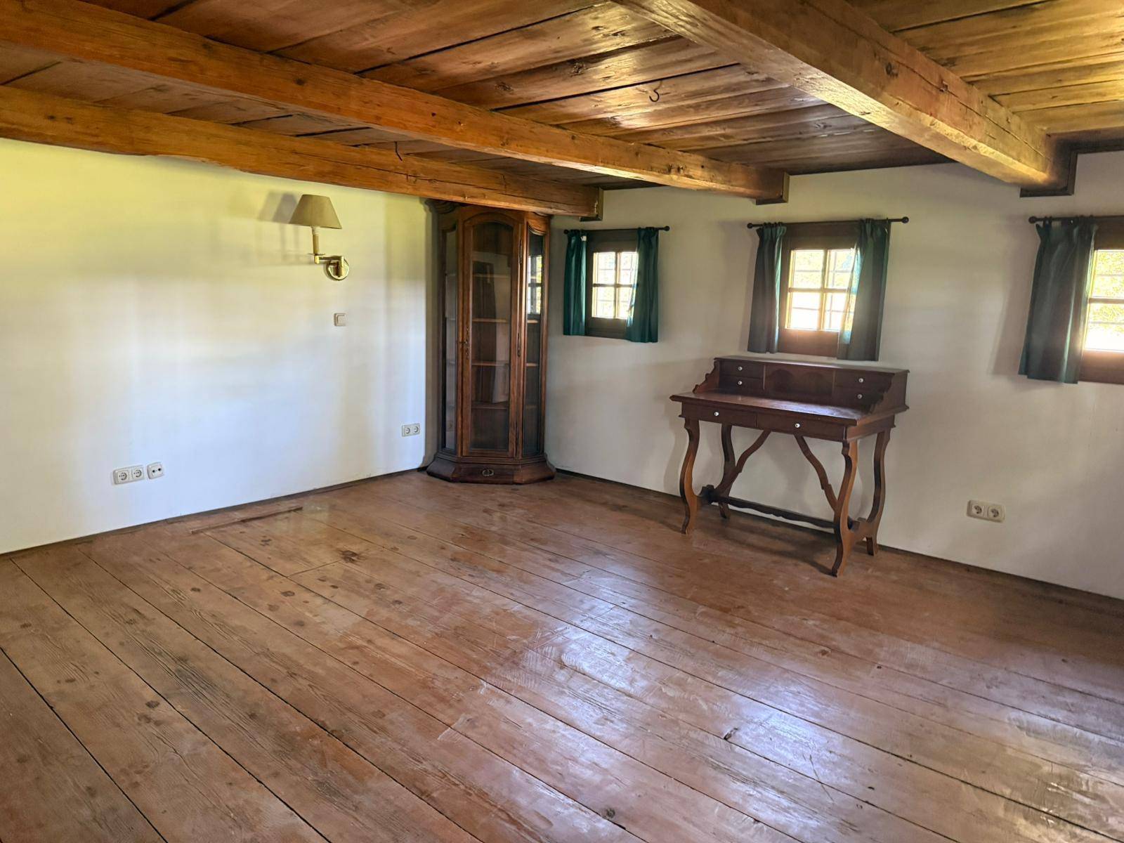 Heller Wohnraum mit Holzbalkendecke, Dielenboden und traditionellen Fenstern, bereit zur Einrichtung.