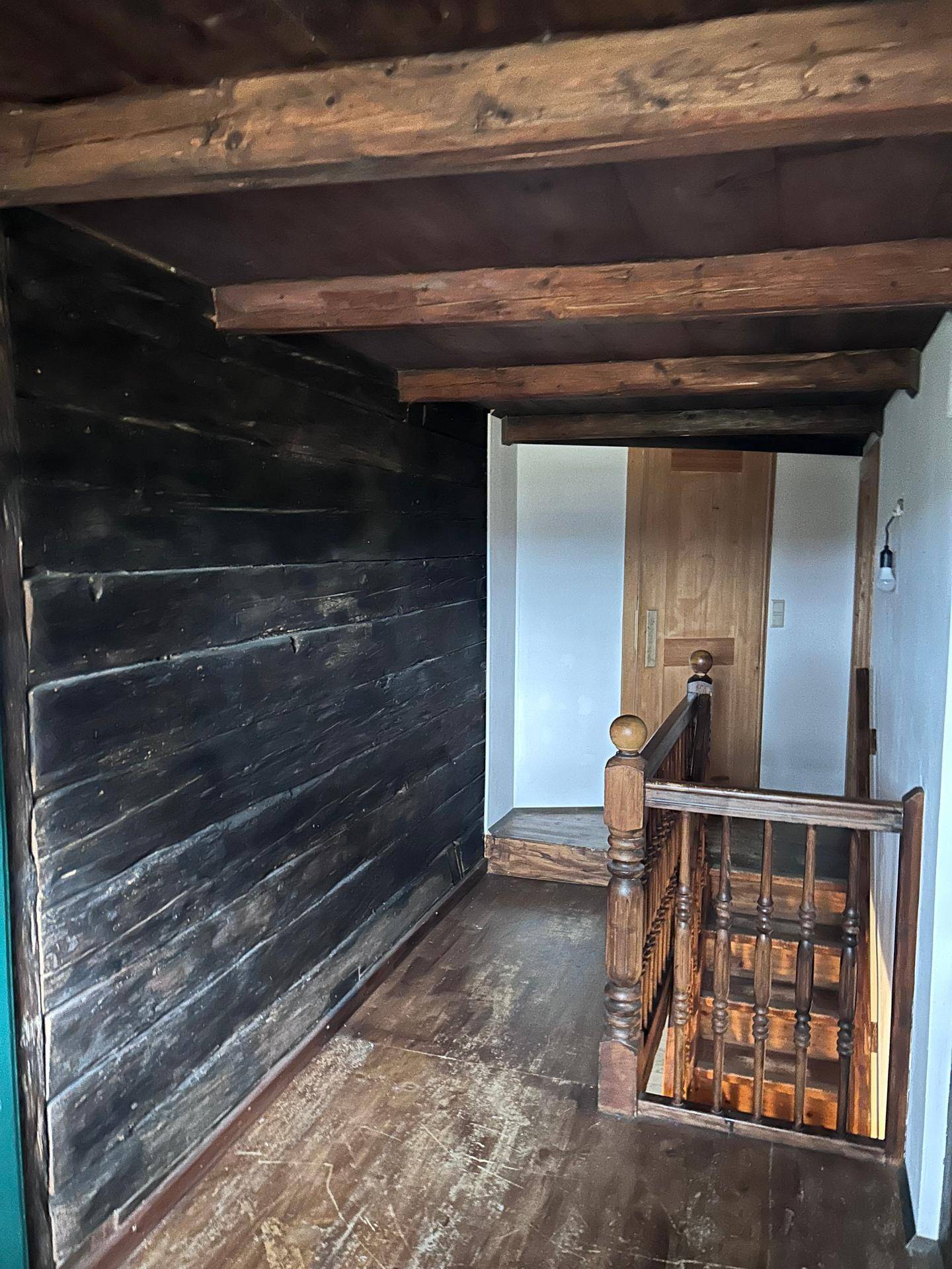 Oberer Flur mit rustikalen Holzbalken und einer traditionellen Holztreppe, die nach unten führt.
