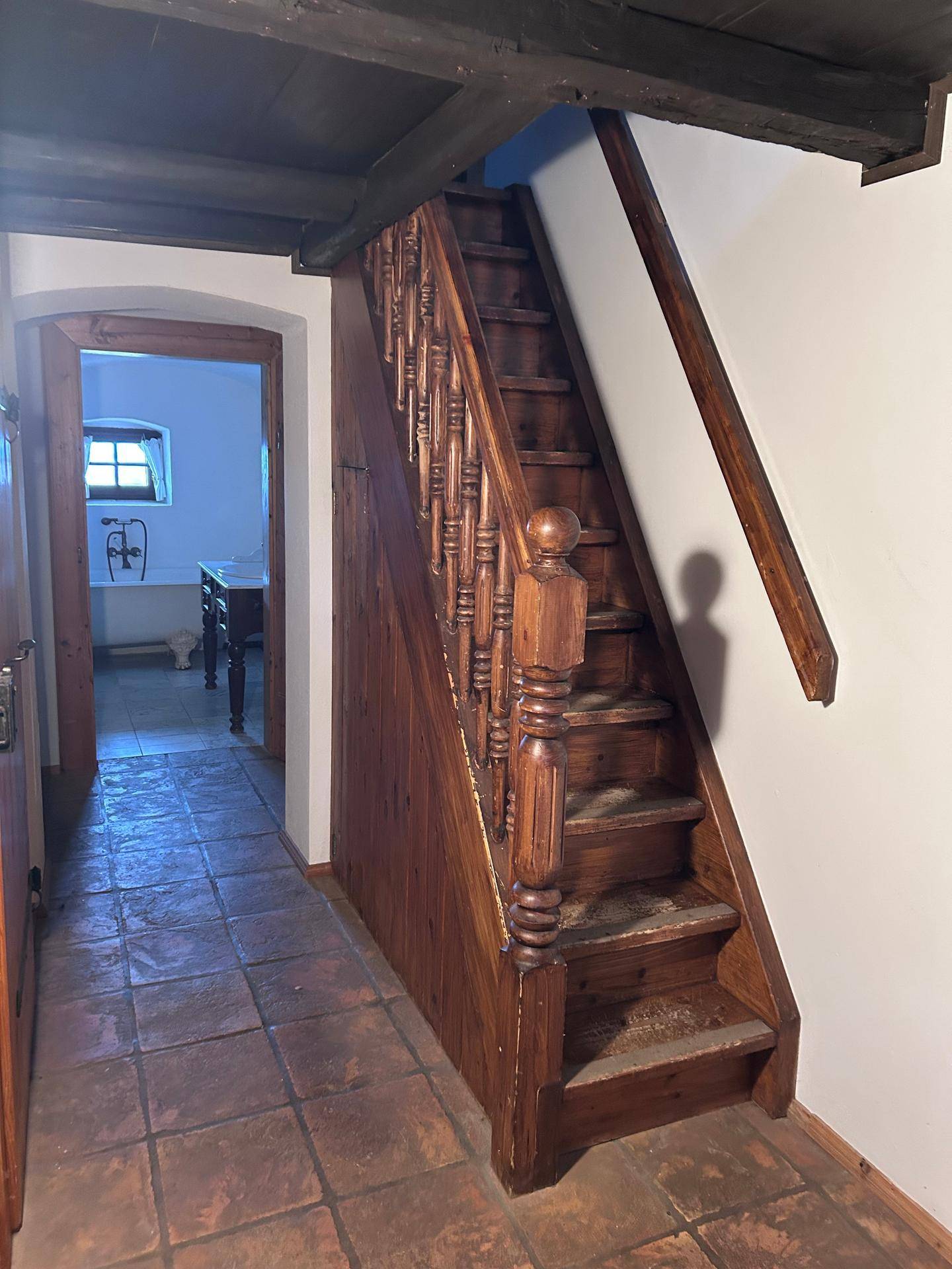 Traditionelle Holztreppe mit gedrechseltem Geländer und Terrakottafliesen im Eingangsbereich.