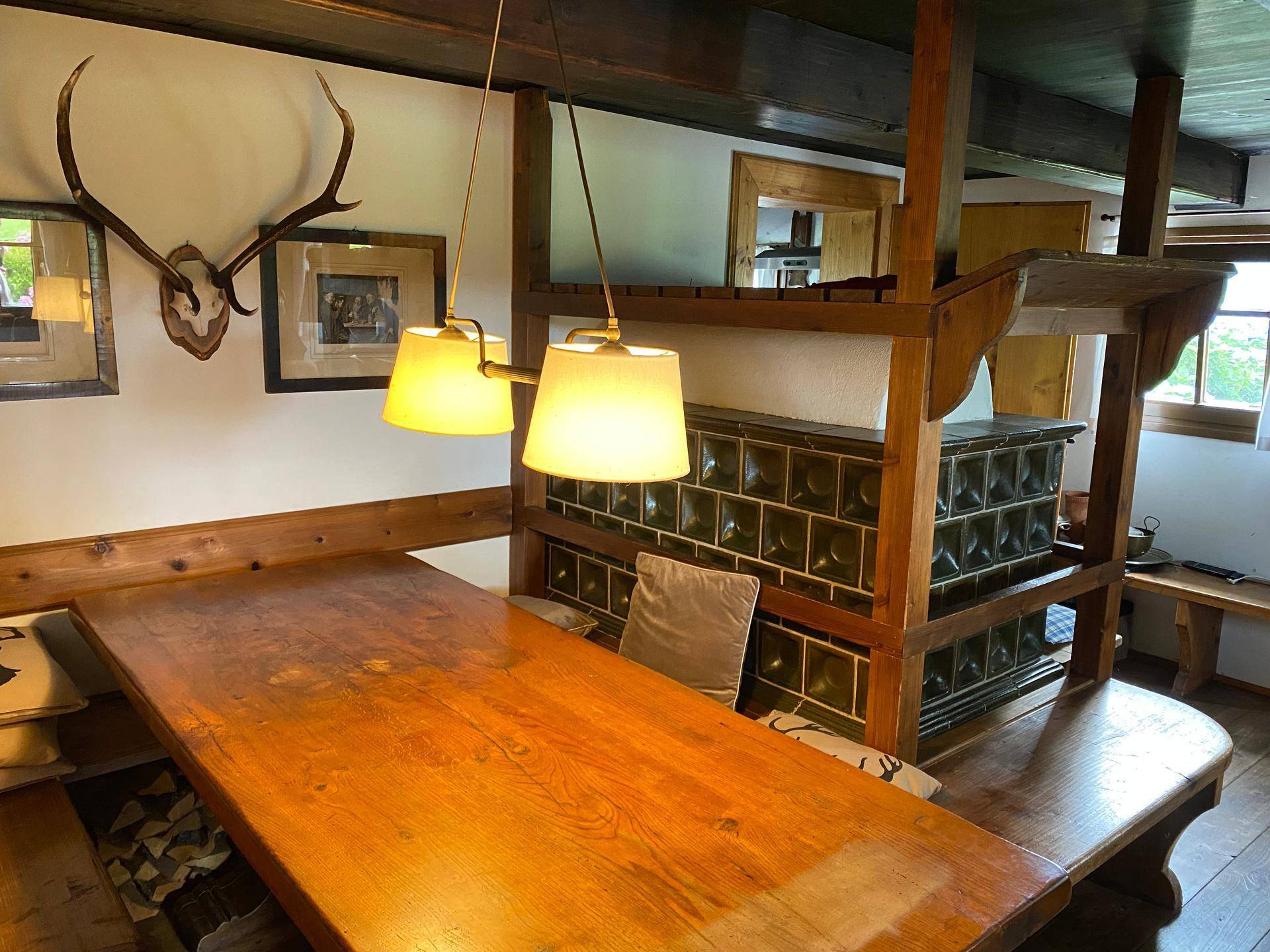 Gemütlicher Essbereich mit Holztisch, Eckbank und traditionellem Kachelofen, dekoriert mit Hirschgeweih.