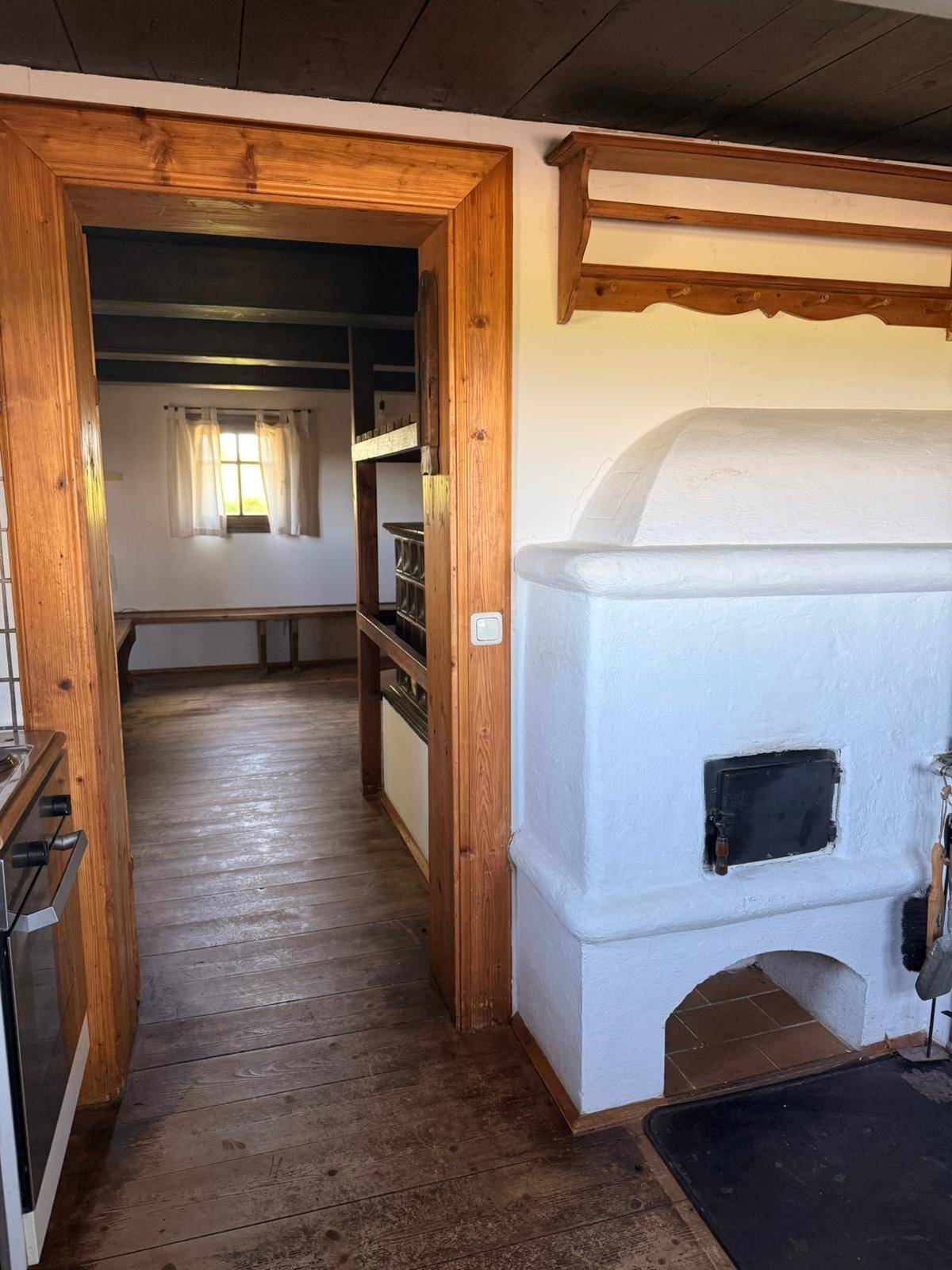 Blick von der Küche in einen angrenzenden Raum mit traditionellem Kachelofen und Holzdielenboden.