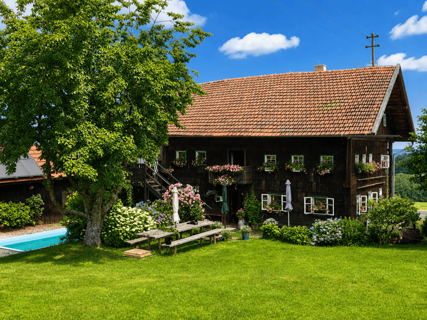 Traditionelles Holzhaus mit Blumenkästen, umgeben von einem gepflegten Garten und einem Pool.