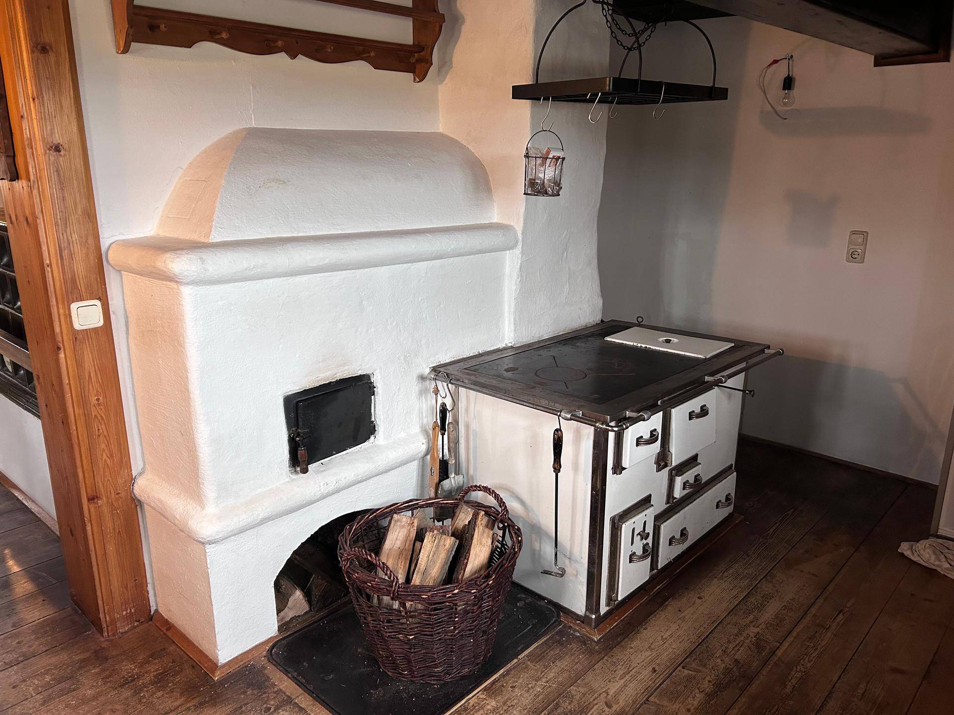 Traditionelle Küche mit weißem Kachelofen und einem Holzherd, bereit zum Kochen und Heizen.