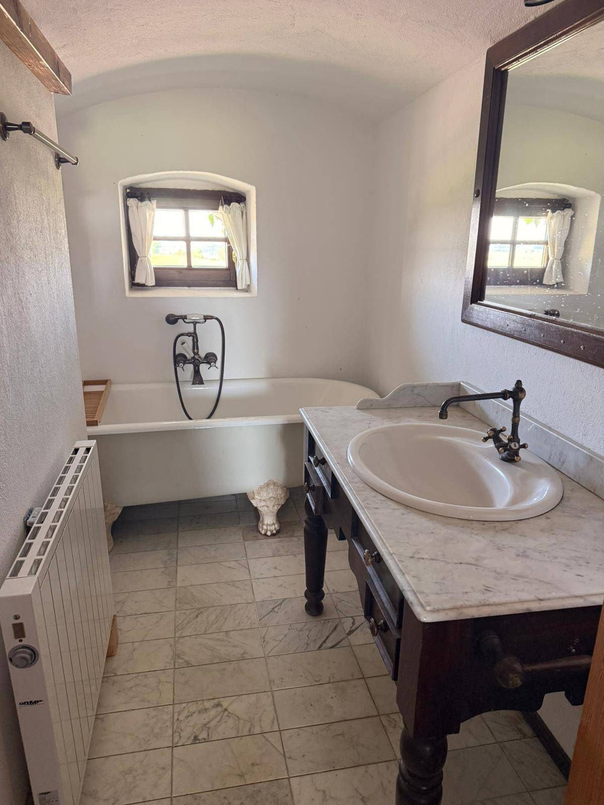 Badezimmer mit freistehender Badewanne, Marmorfliesen und einem Waschtisch mit antikem Charme.