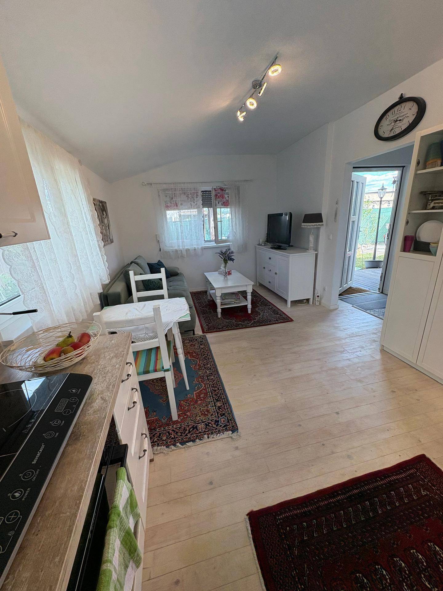Offener Wohn- und Essbereich mit kleiner Küche, Sofa und Esstisch auf hellem Holzboden.