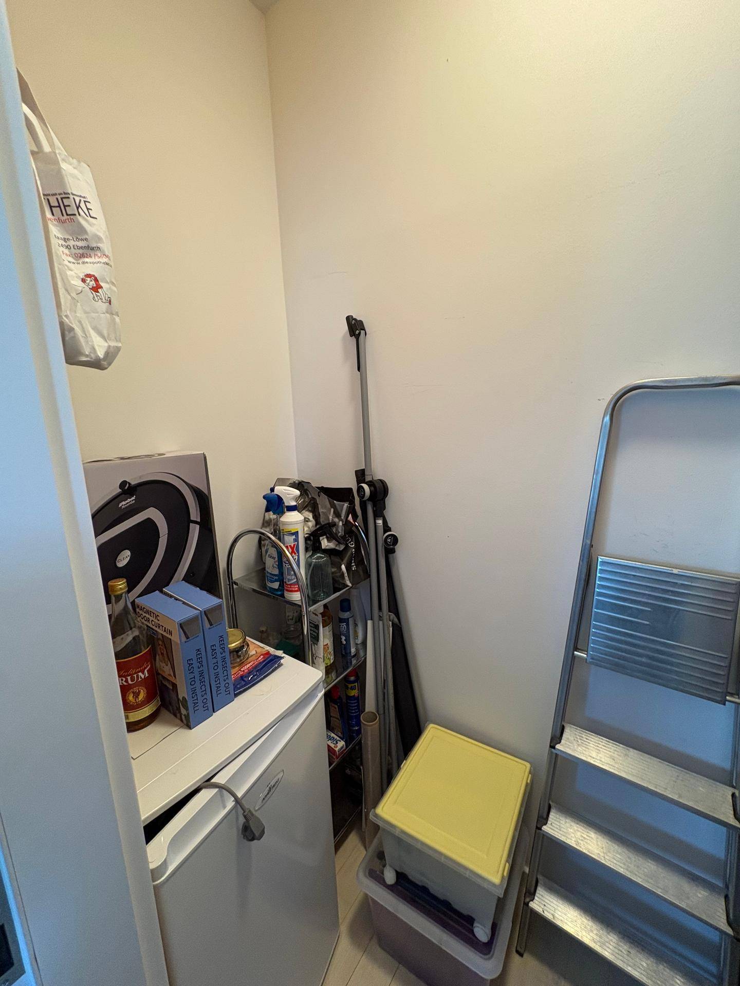Kleiner Abstellraum mit Reinigungsutensilien, Leiter und einem kleinen Kühlschrank.