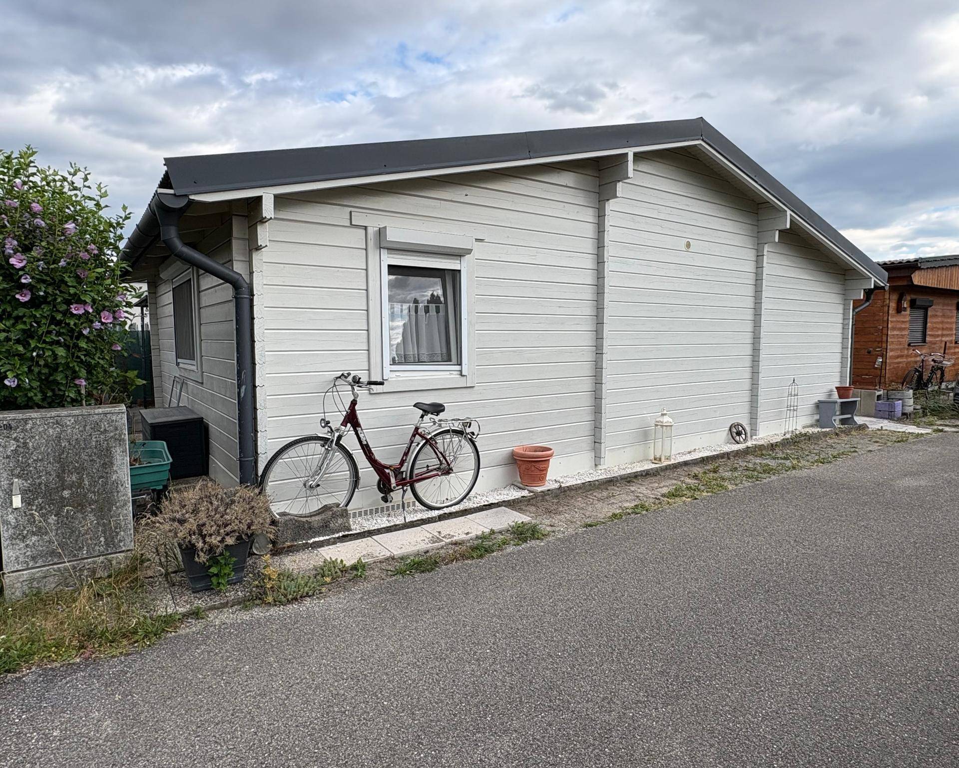 Seitenansicht des kleinen Hauses mit heller Holzfassade und einem Fahrrad davor abgestellt.