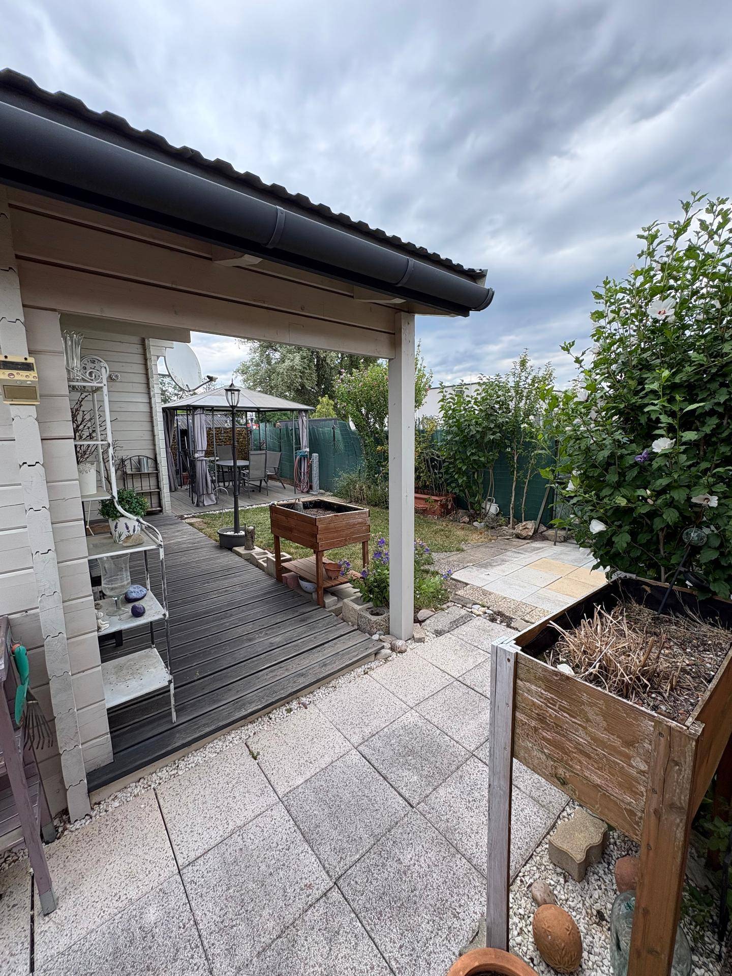 Überdachte Holzterrasse mit Blick auf den Garten und einen weiteren Sitzbereich im Hintergrund.