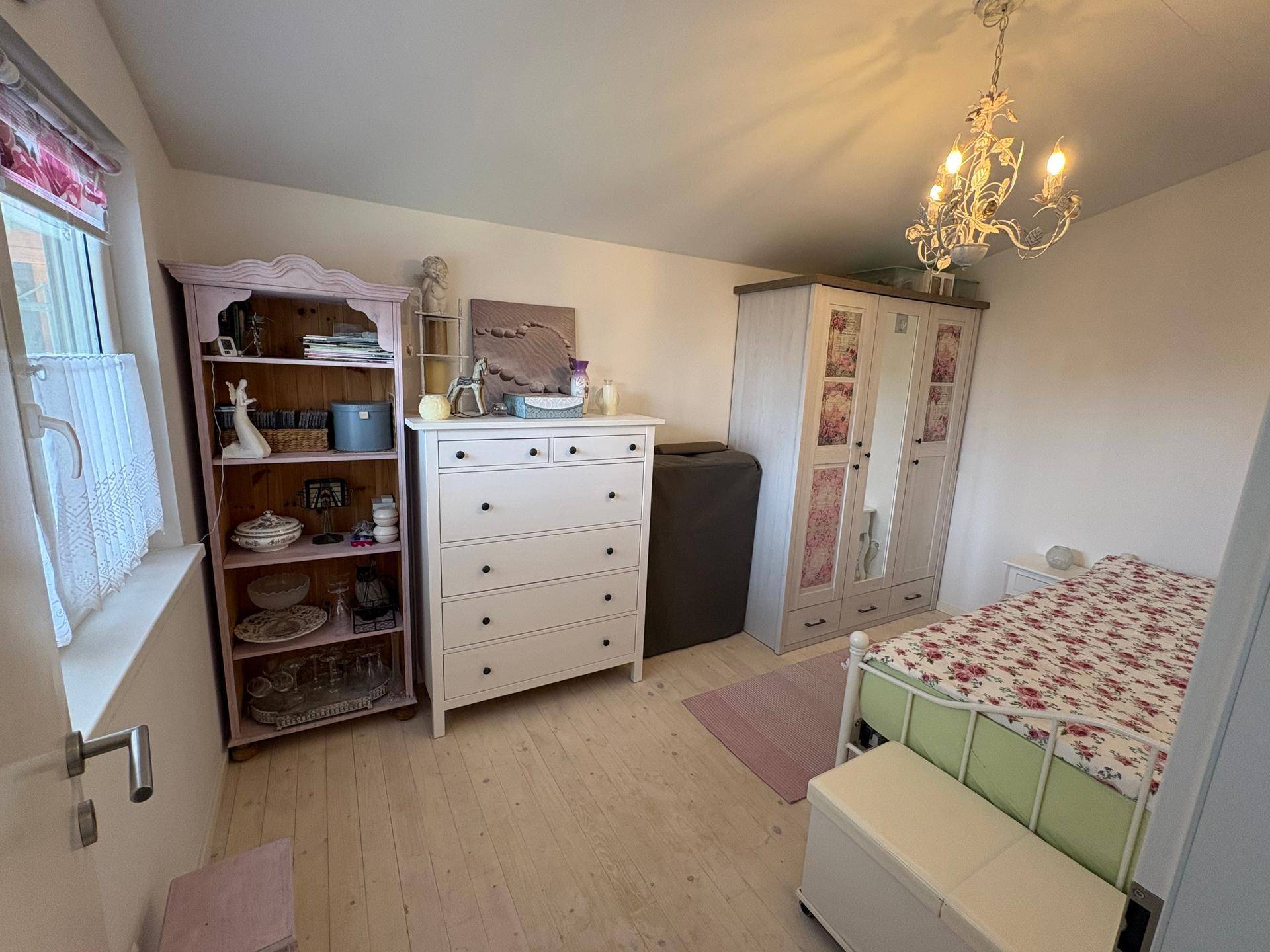 Gemütliches Schlafzimmer mit Einzelbett, Kommode und Schrank auf hellem Holzboden.