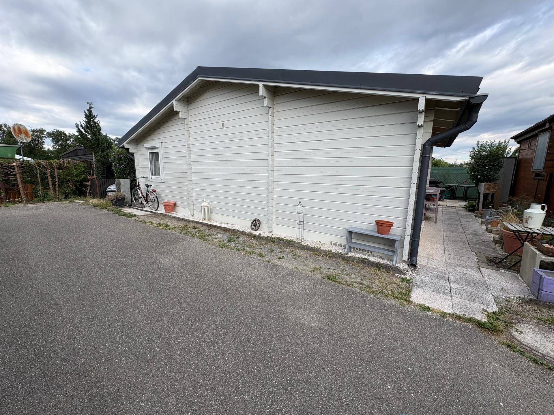 Seitenansicht des kleinen Hauses mit heller Holzfassade und einem gepflasterten Zugangsweg.