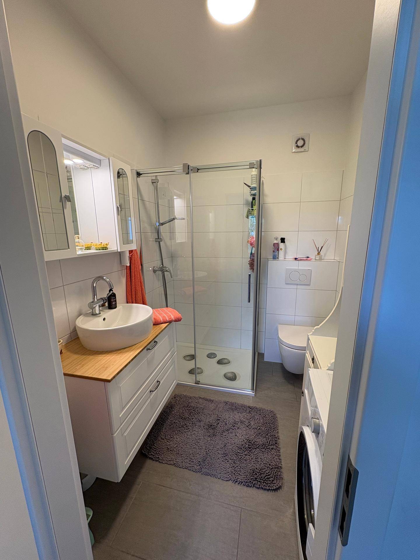 Modernes Badezimmer mit Duschkabine, Waschbecken und WC auf grauem Fliesenboden.