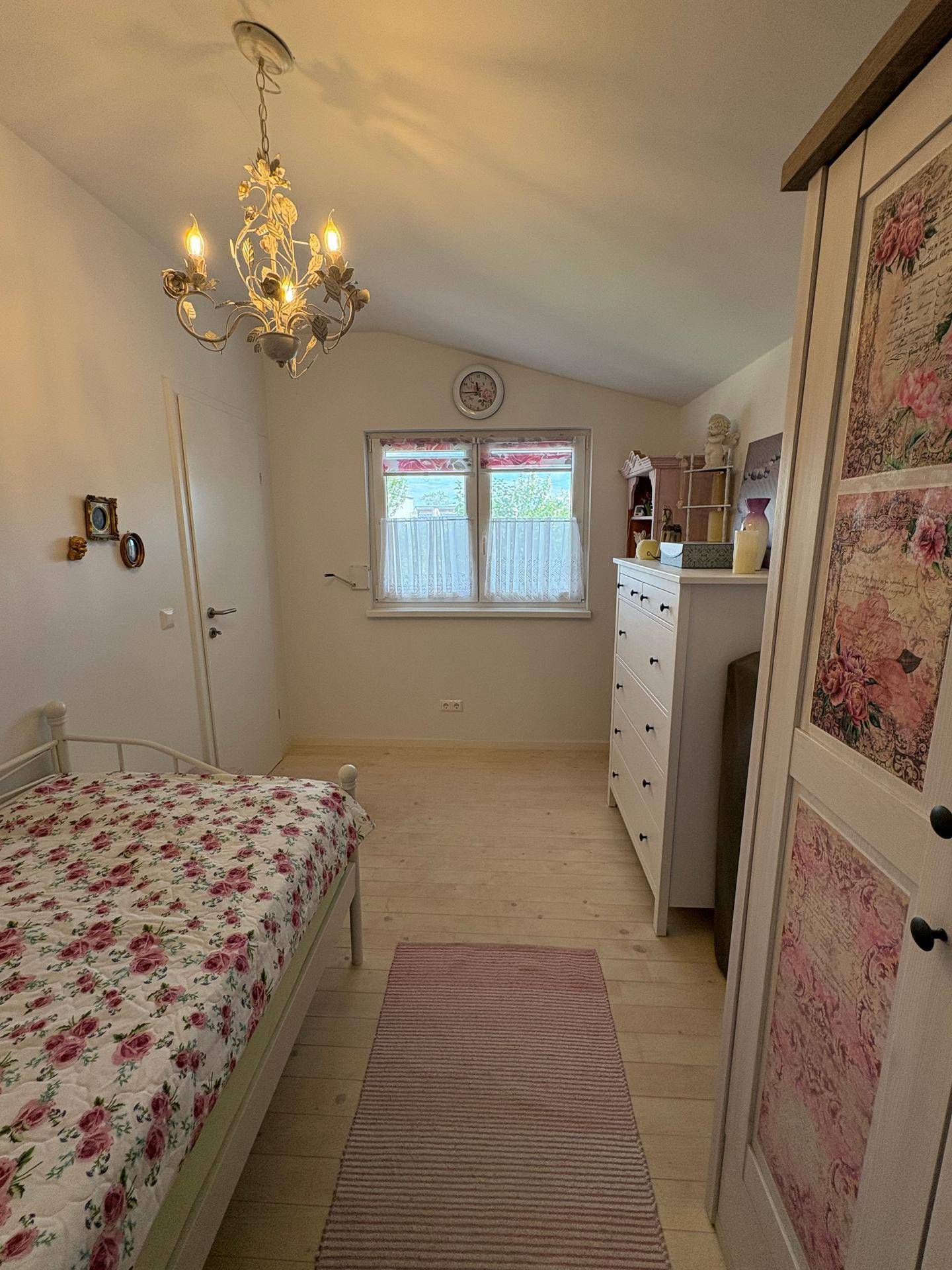 Helles Schlafzimmer mit Einzelbett, Fenster und einem dekorativen Kronleuchter an der Decke.
