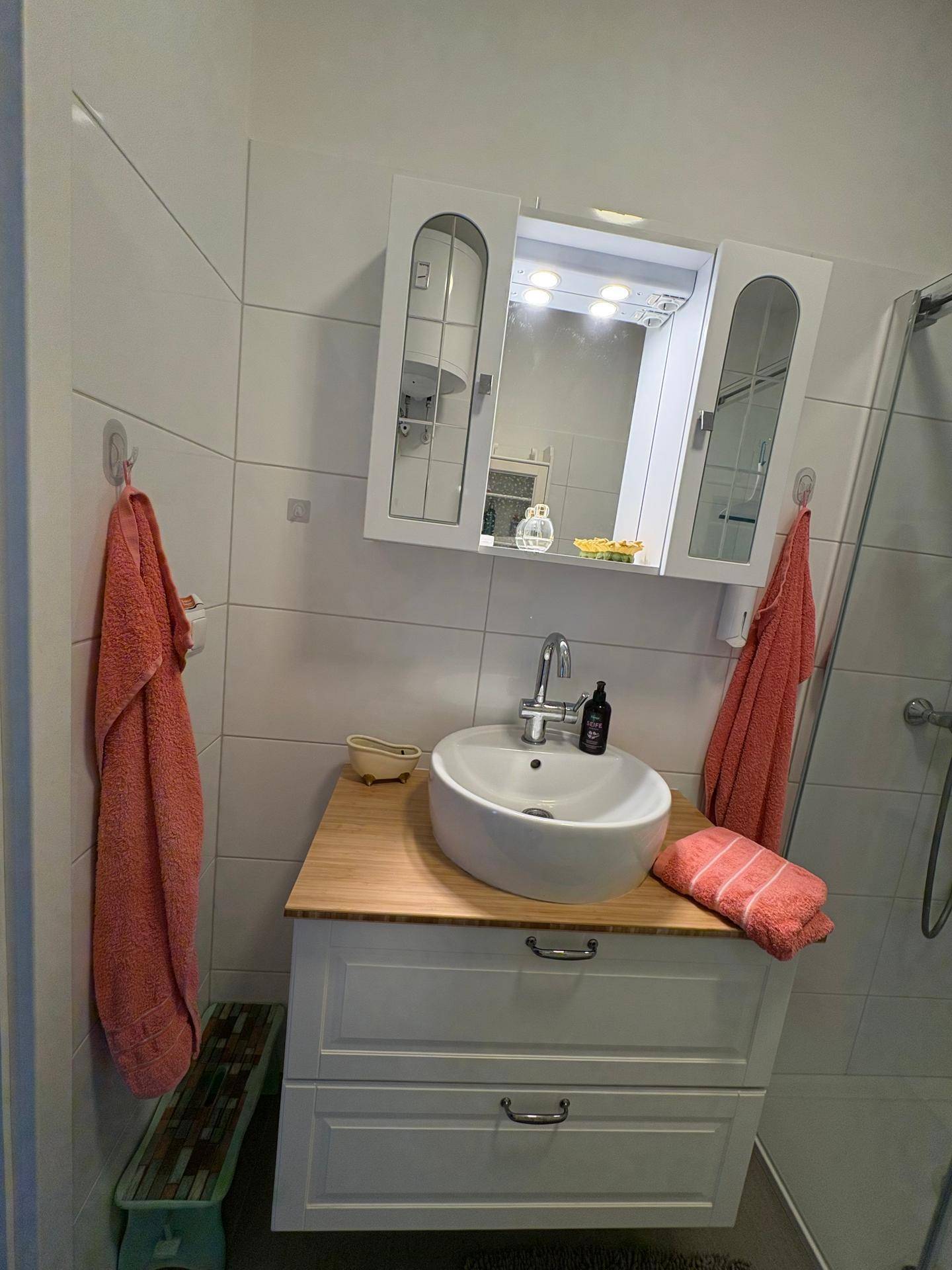 Helles Badezimmer mit modernem Waschbecken, Spiegelschrank und Handtüchern.
