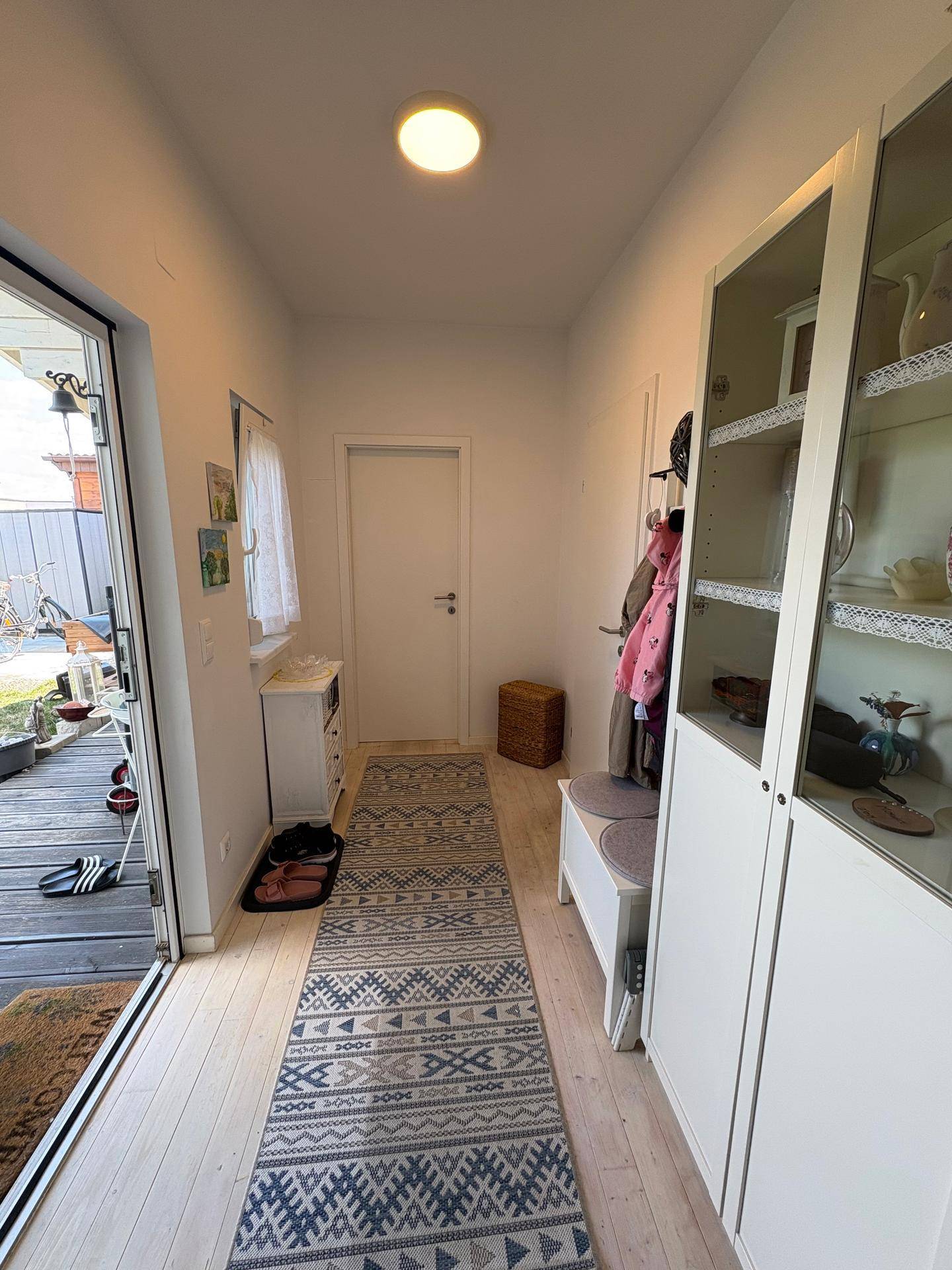 Langer, heller Flur mit Holzboden, Garderobe und Blick auf den Garten durch die Glastür.
