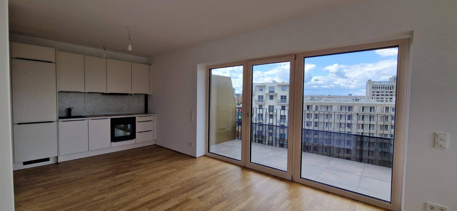 Heller offener Wohn-Essbereich mit integrierter Küche, Parkettboden und Zugang zu einem großen Balkon.