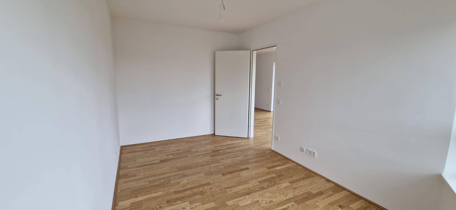 Helles Schlafzimmer mit Parkettboden und weiß gestrichenen Wänden, bereit zur Einrichtung.