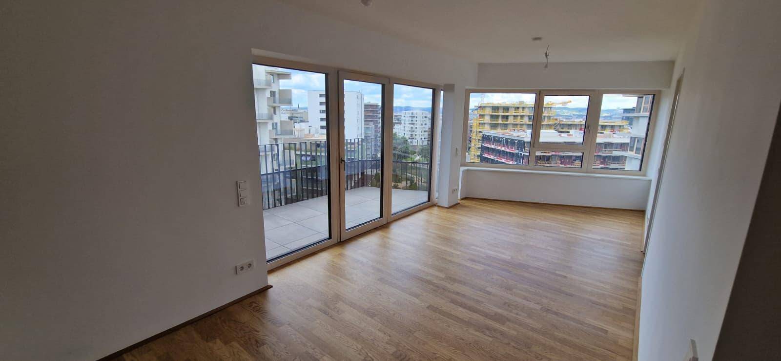 Geräumiger Wohnbereich mit Parkettboden, großen Fenstern und Zugang zum Balkon.