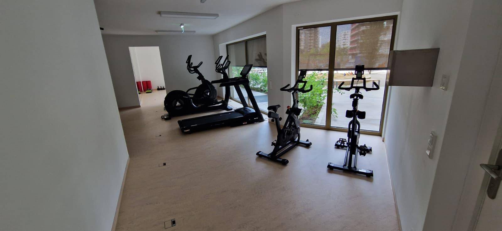 Gemeinschaftlicher Fitnessraum mit modernen Geräten und großen Fenstern.
