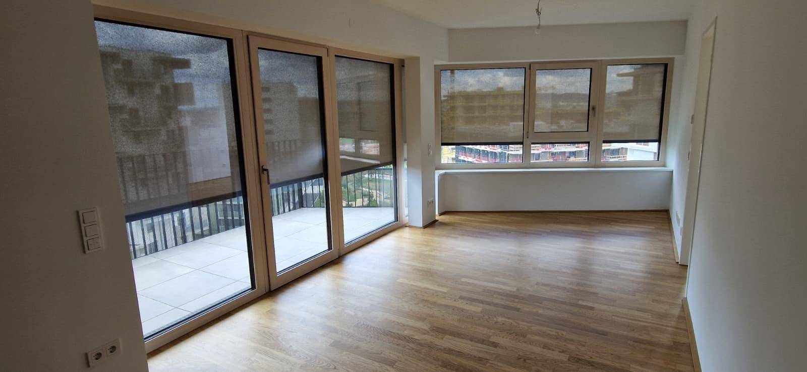 Geräumiges Wohnzimmer mit großen Fenstern, Parkettboden und Zugang zu einem Balkon.