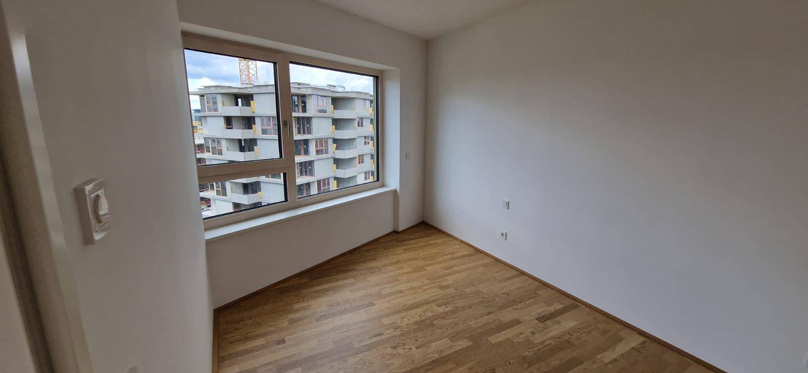 Schlafzimmer mit Parkettboden und großem Fenster, das viel Tageslicht hereinlässt.