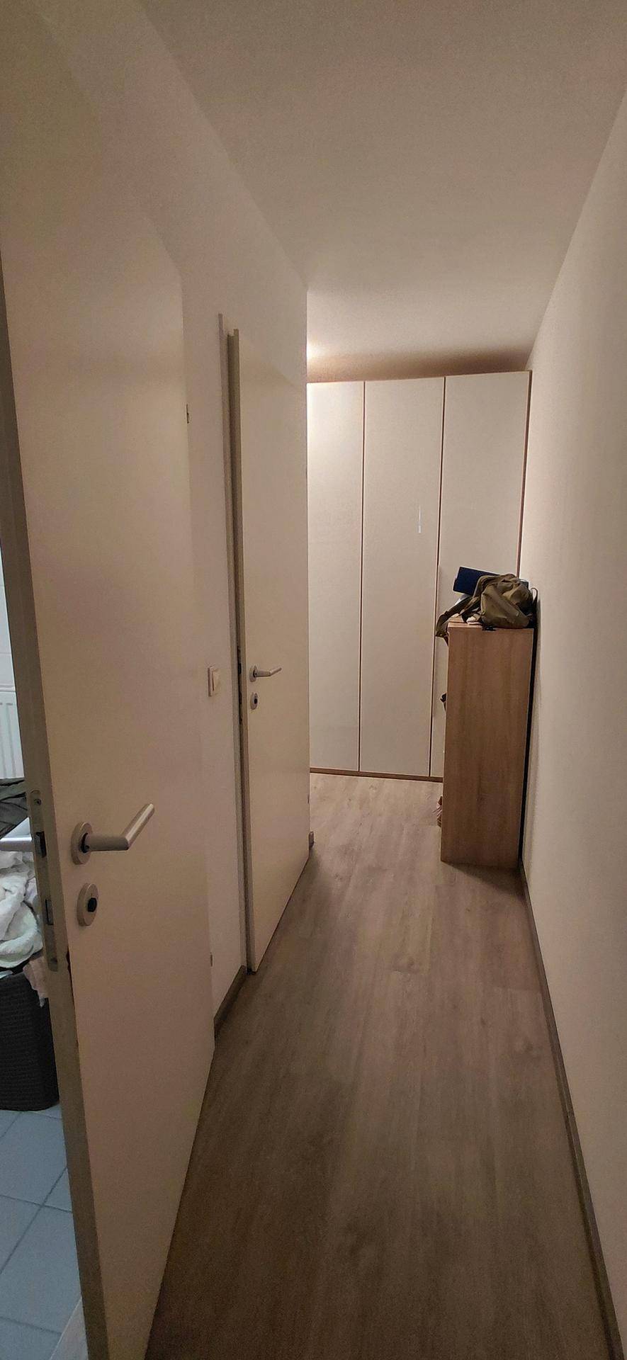 Heller Flur mit Holzboden, weißen Türen und einem Einbauschrank am Ende des Ganges.