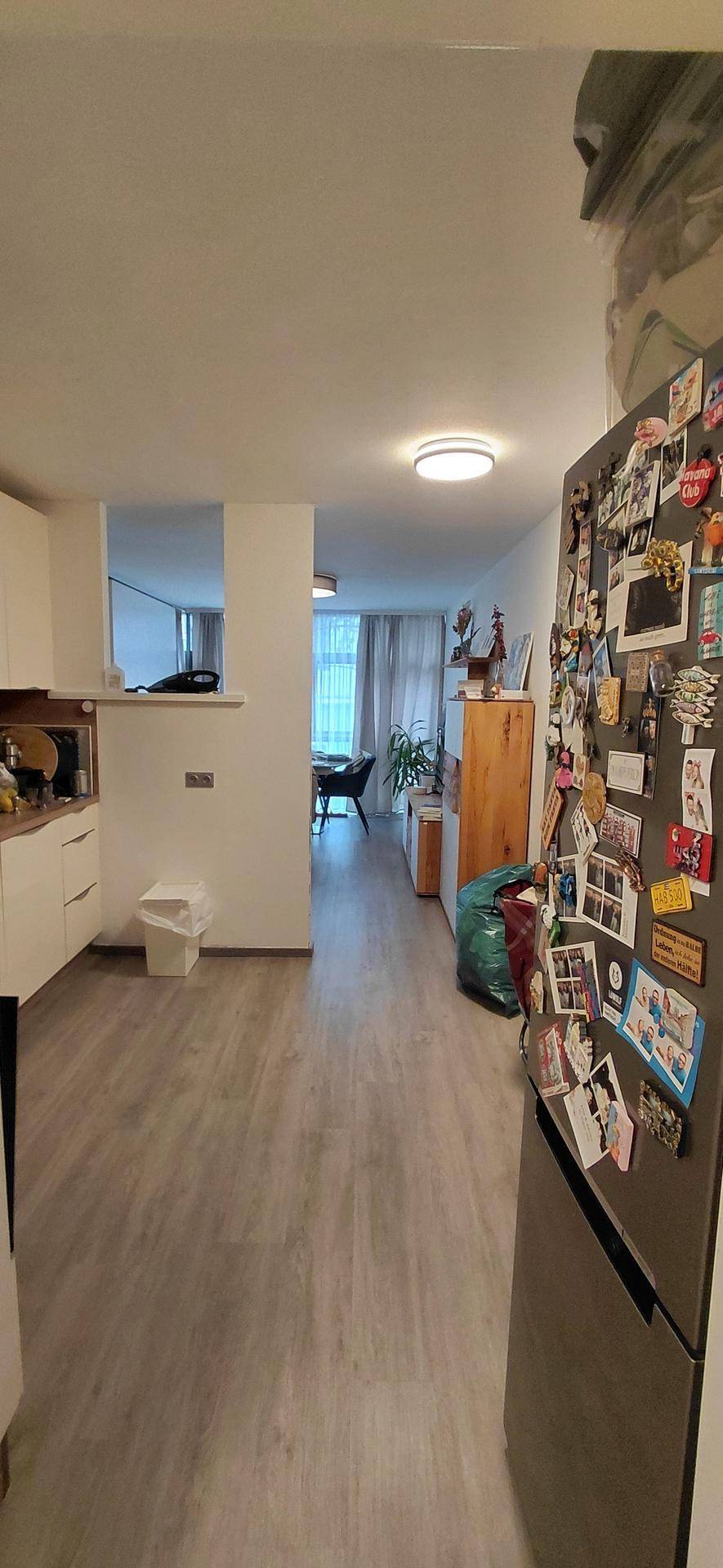 Offener Wohnbereich mit Holzboden, der zum Essbereich und den großen Fenstern führt, inklusive Kühlschrank.