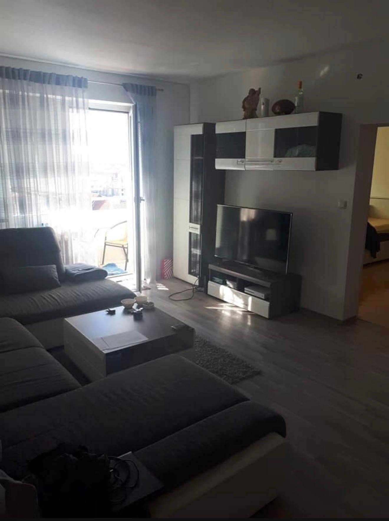 Helles Wohnzimmer mit großem Ecksofa, Fernseher und Zugang zu einem Balkon.