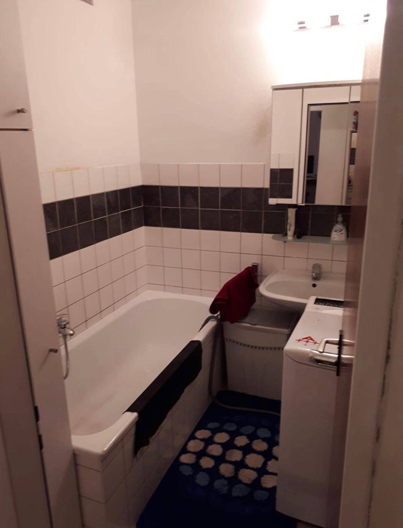 Badezimmer mit Badewanne, Waschbecken und Wandfliesen in Weiß und Dunkelgrau.