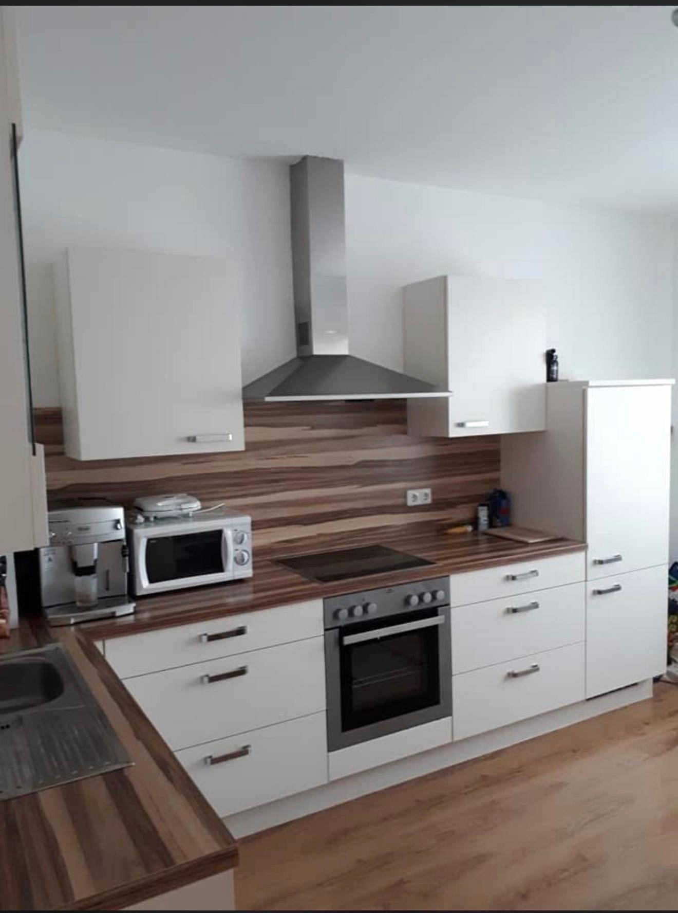 Moderne Einbauküche mit weißen Schränken, Holzoptik-Arbeitsplatten und integrierten Geräten.