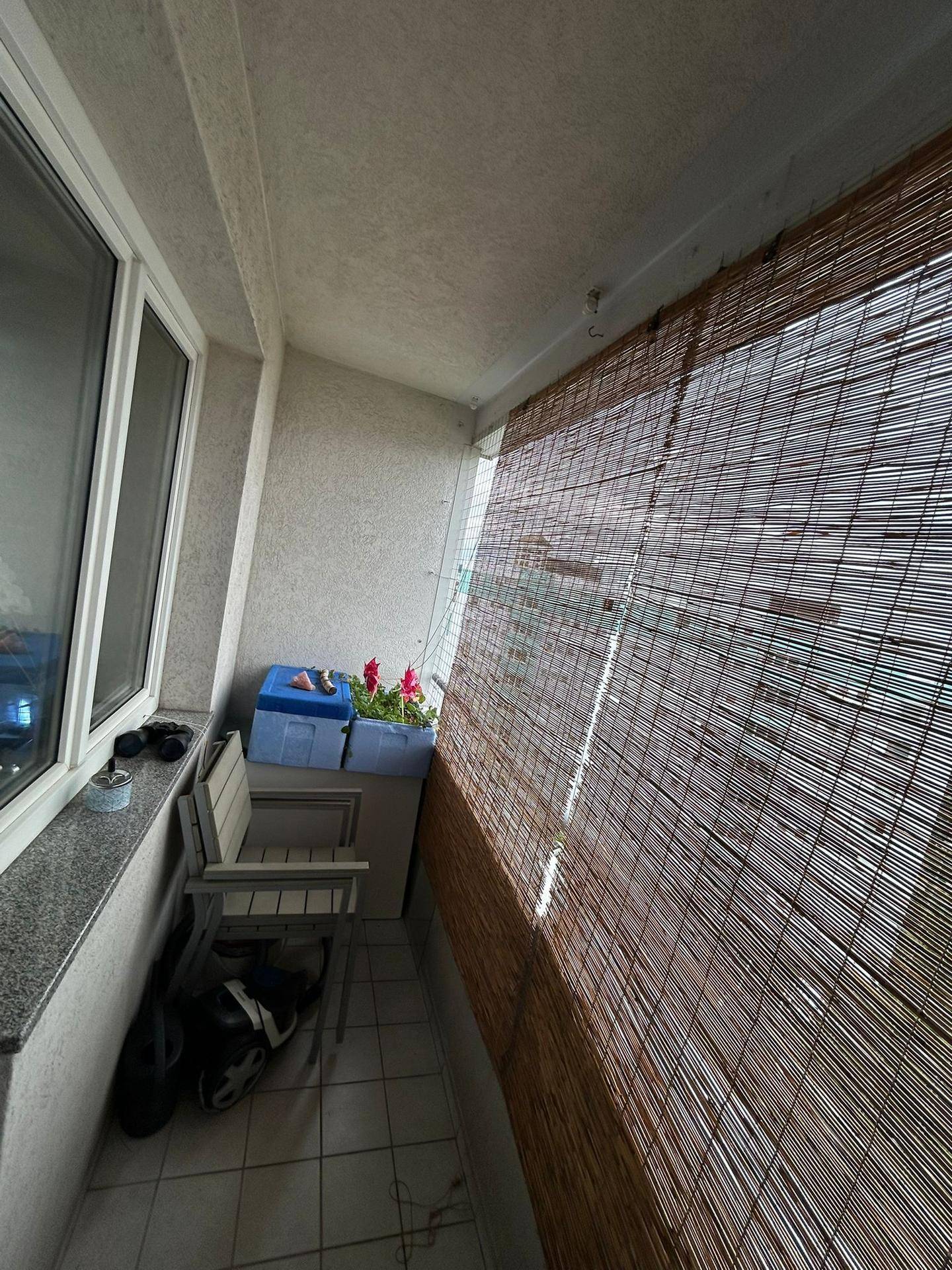 Schmaler Balkon mit Bambus-Sichtschutz, Fliesenboden und einem Stuhl.