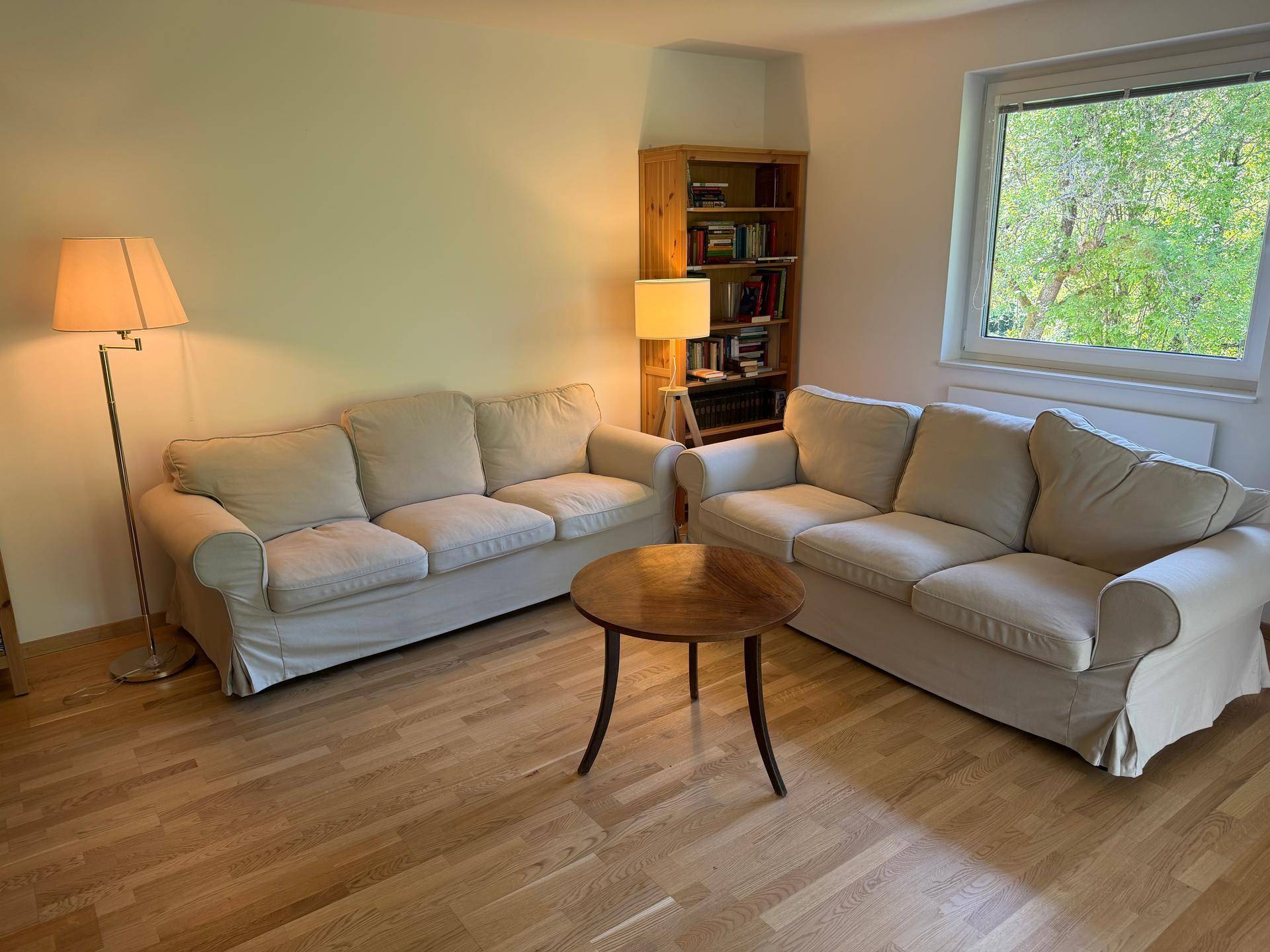 Gemütliches Wohnzimmer mit zwei beigen Sofas, Holzboden und Bücherregal.