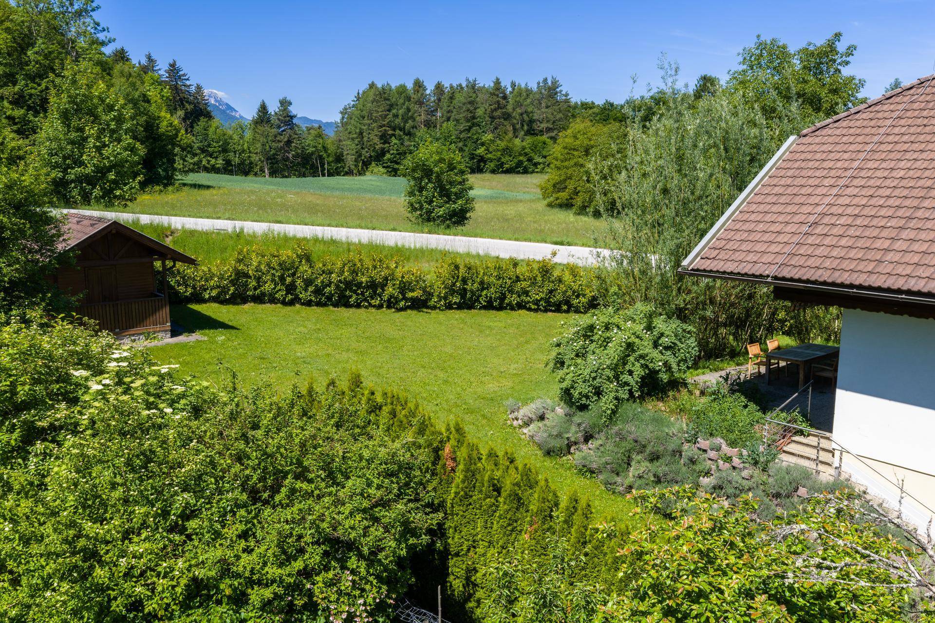 Weitläufiger Gartenbereich mit Rasenfläche, Hecken und einem kleinen Gartenhaus, umgeben von Natur.